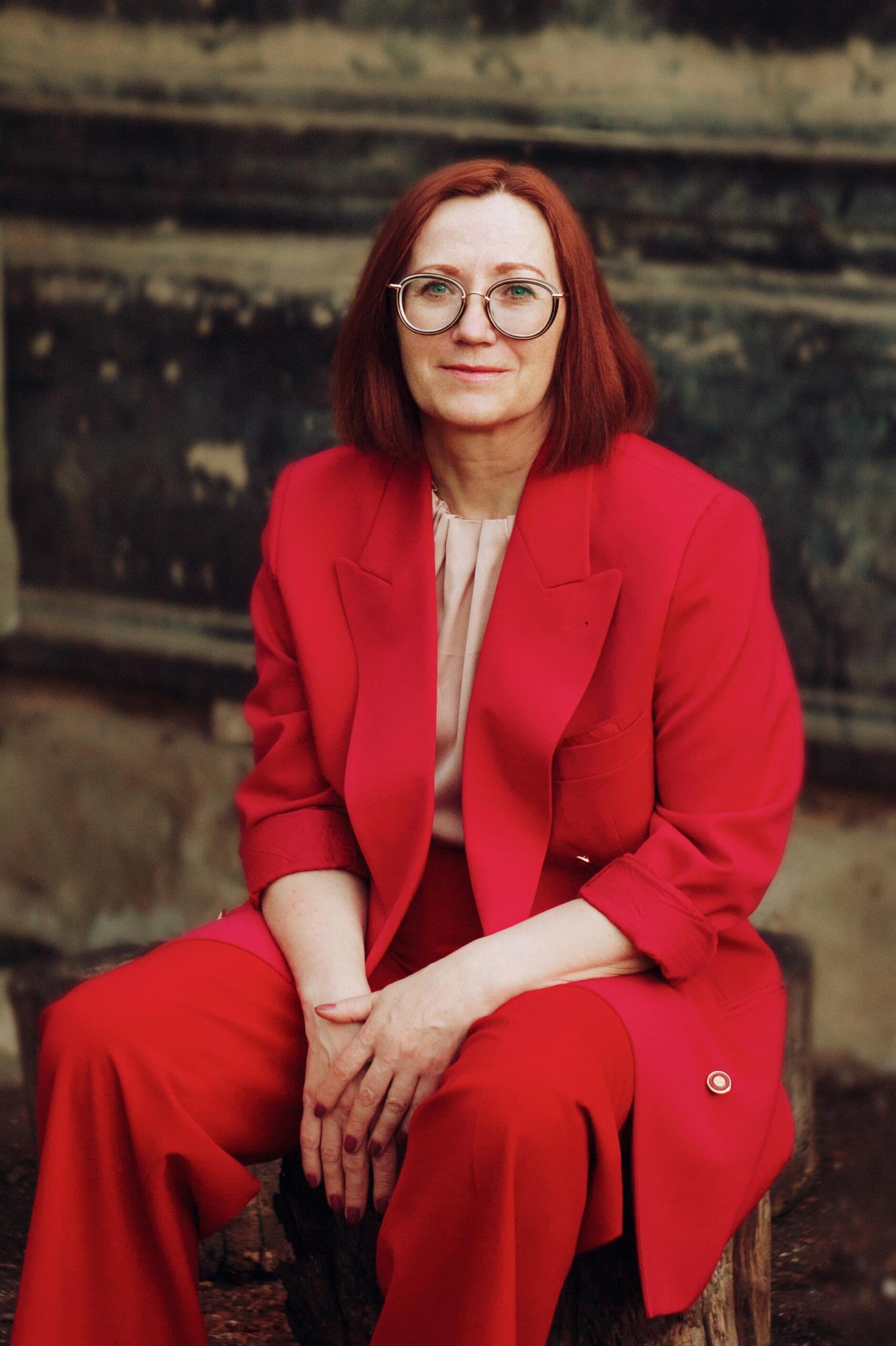 A woman in a red pantsuit wearing glasses. 