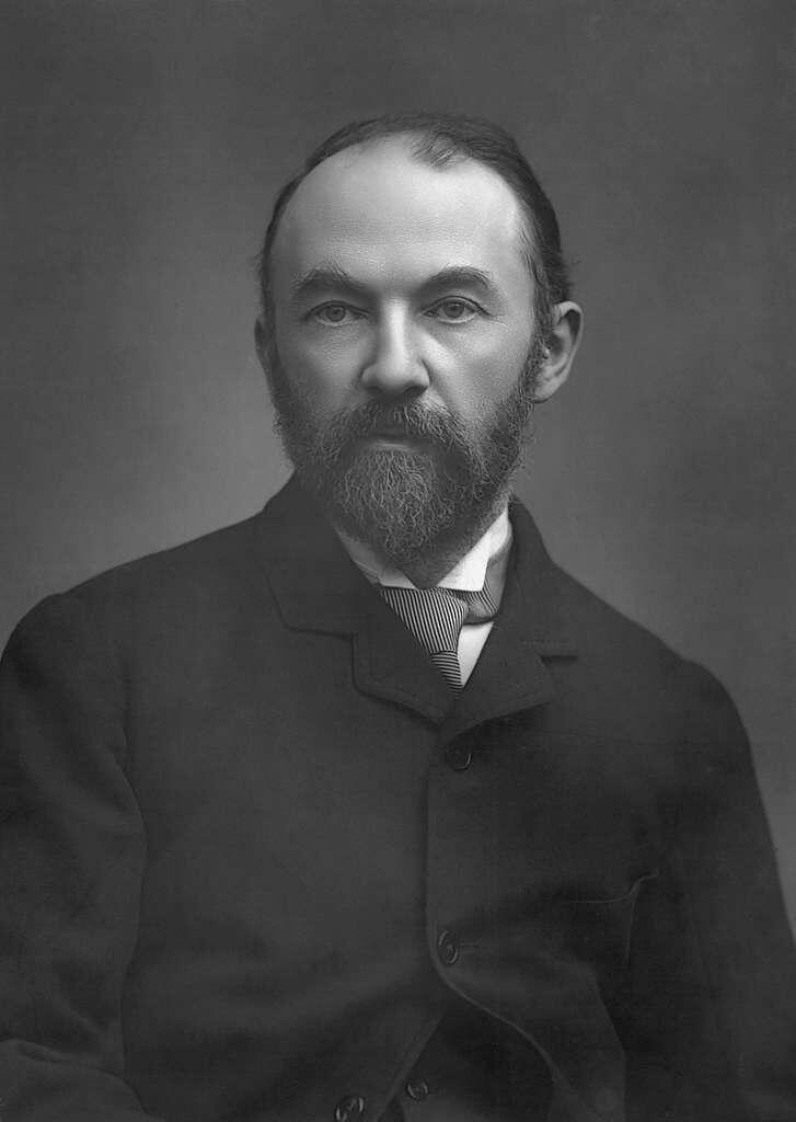 A historical black-and-white portrait of a man in formal attire, featuring a coat and a striped tie, sitting against a gradient background.