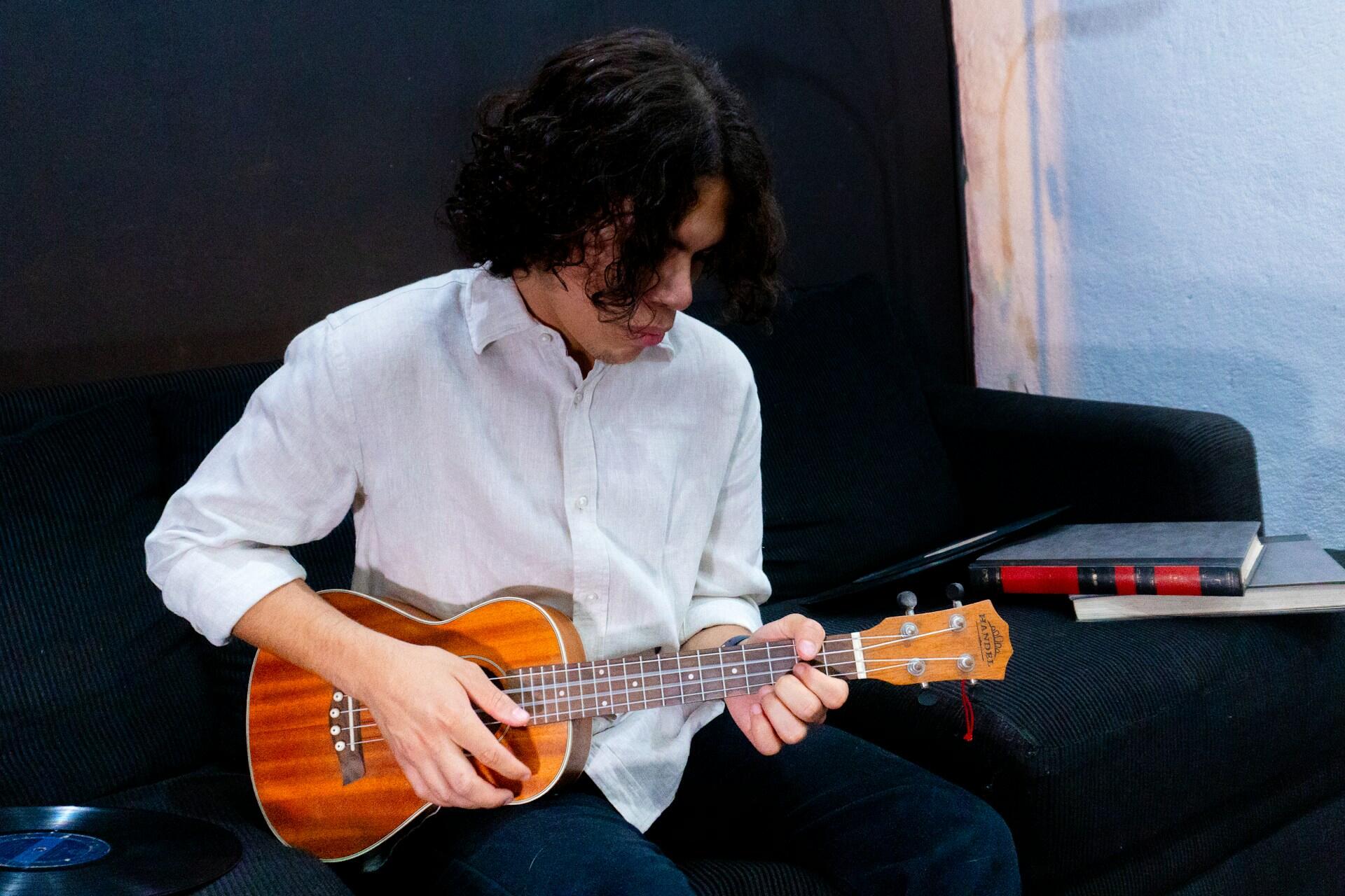 Person seated on a sofa playing a ukulele while looking at the fretboard.