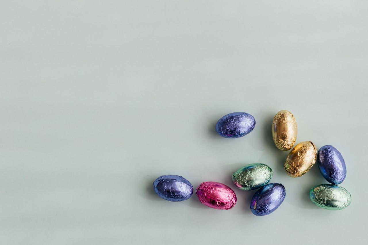 A collection of colorful, shiny chocolate Easter eggs arranged on a light gray surface.