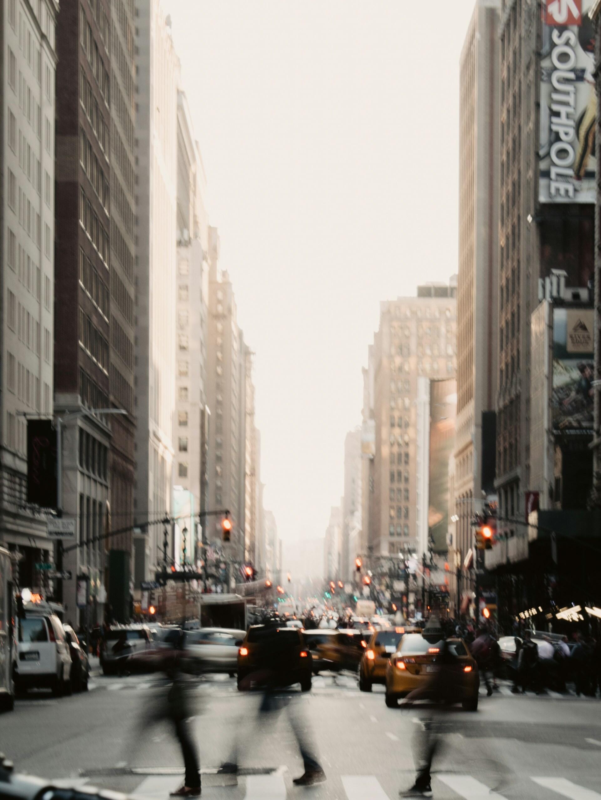 A city street with one-way traffic and people in a crosswalk. 