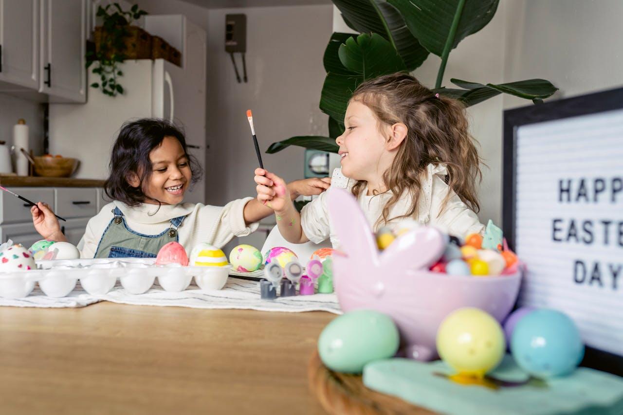Two children paint colorful Easter eggs at a wooden table, surrounded by festive decorations and a 