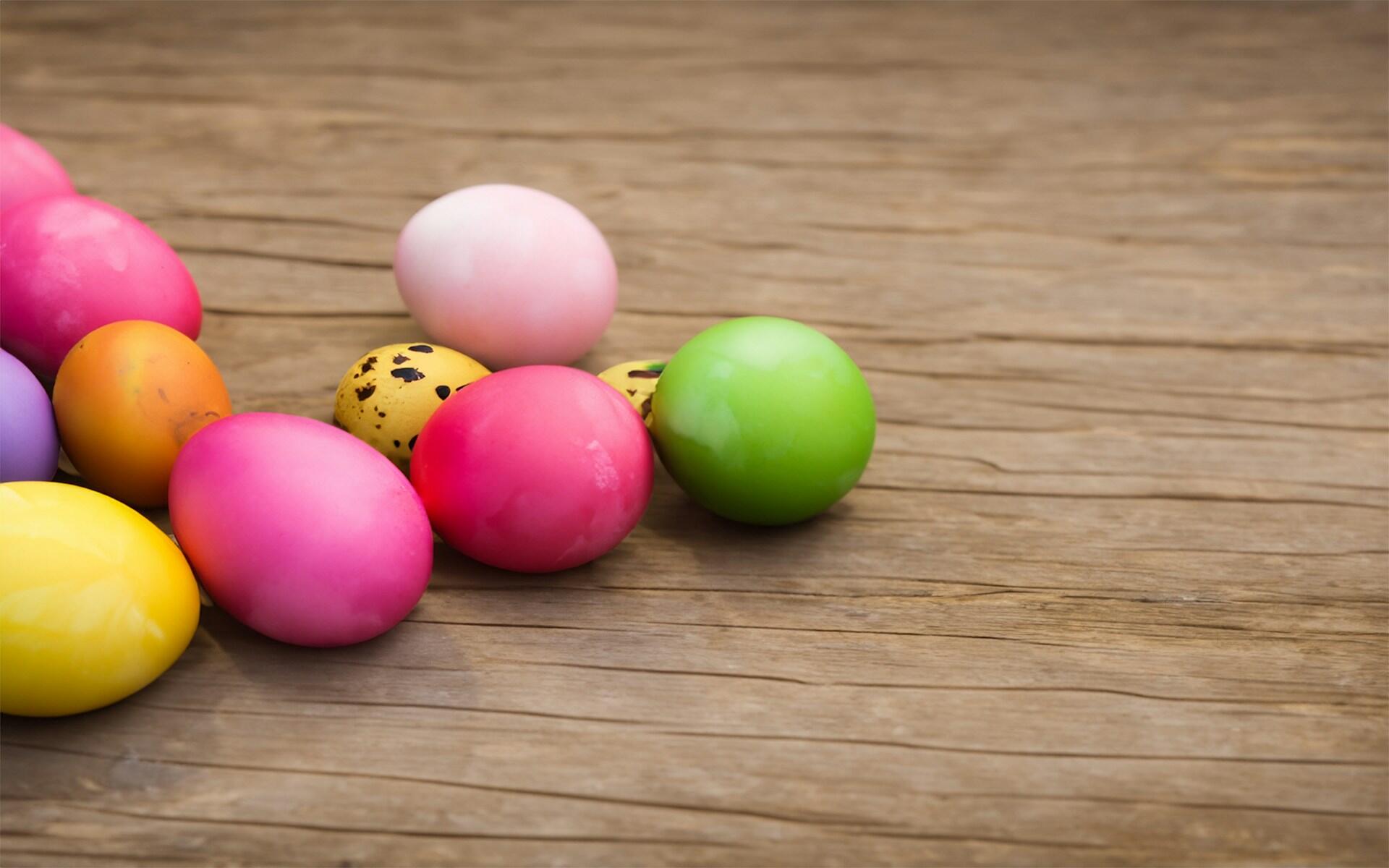 Colourful Easter eggs scattered on a wooden surface, featuring pink, yellow, green, purple, and a speckled egg.