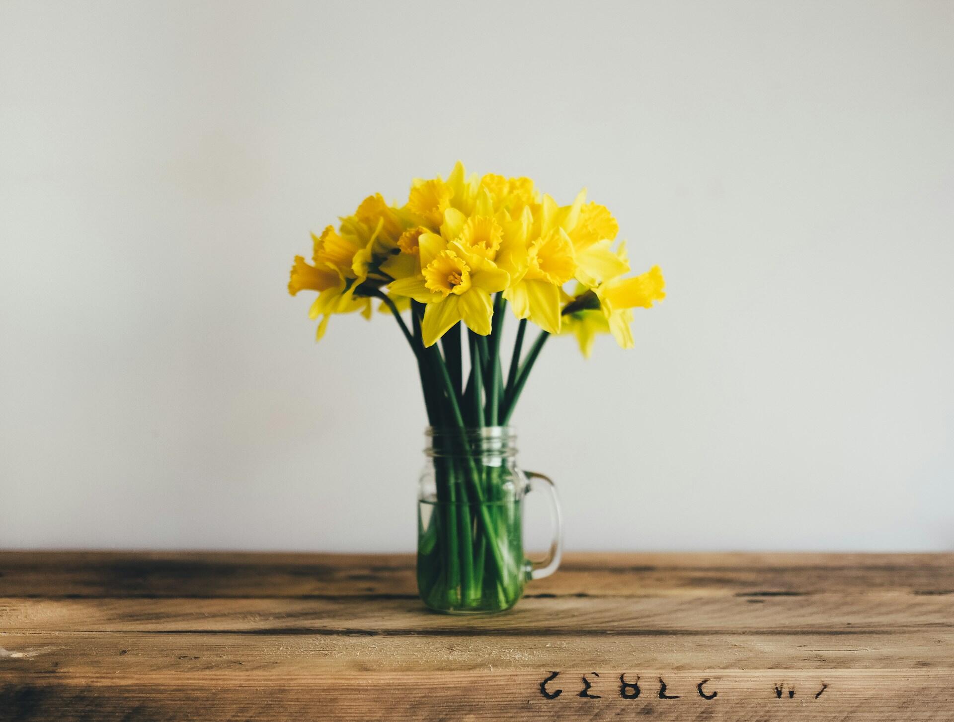 A bouquet of yellow flowers in a glass jar on a wooden table.