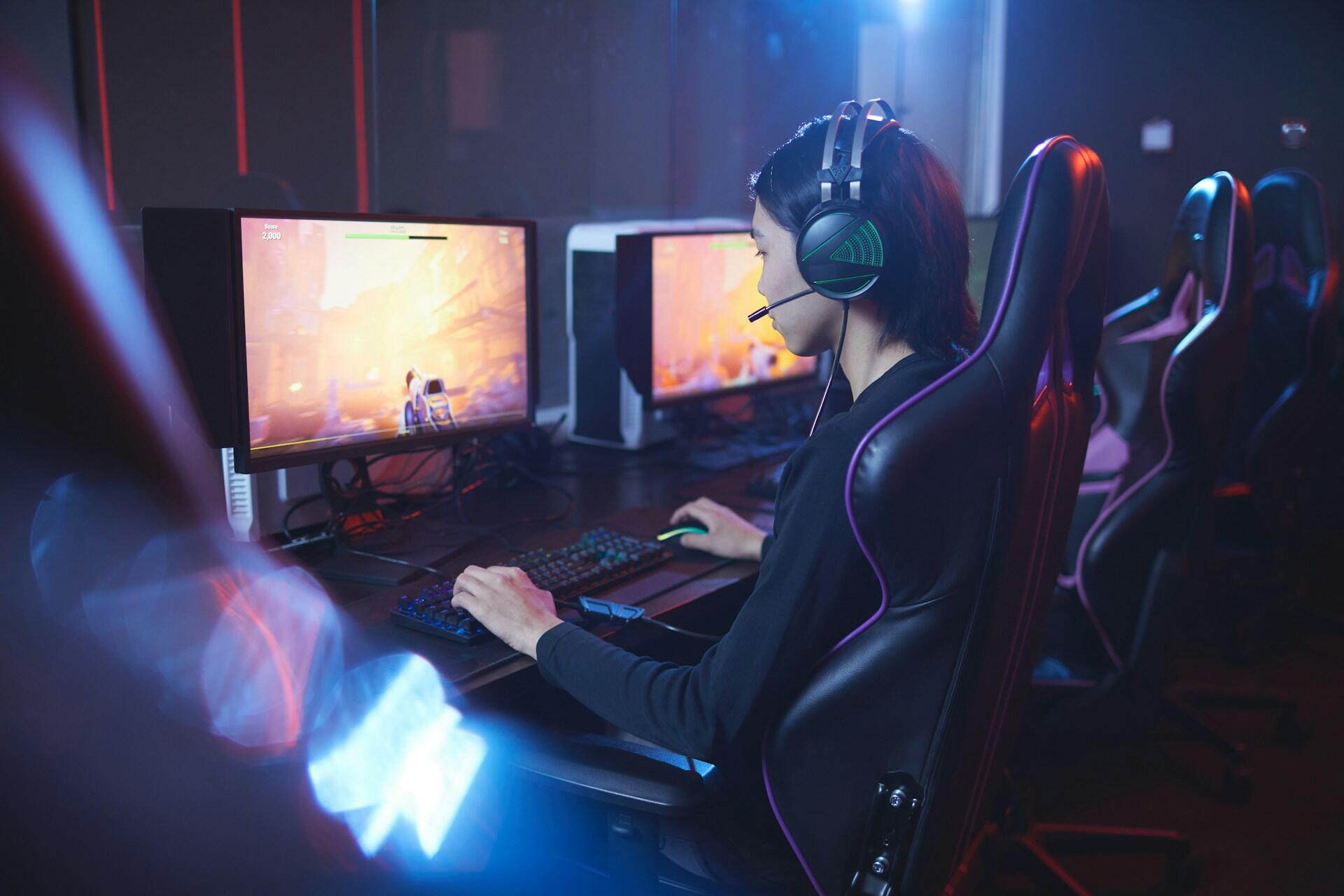 A person in a darkened room in front of a computer, wearing headphones, playing a game.