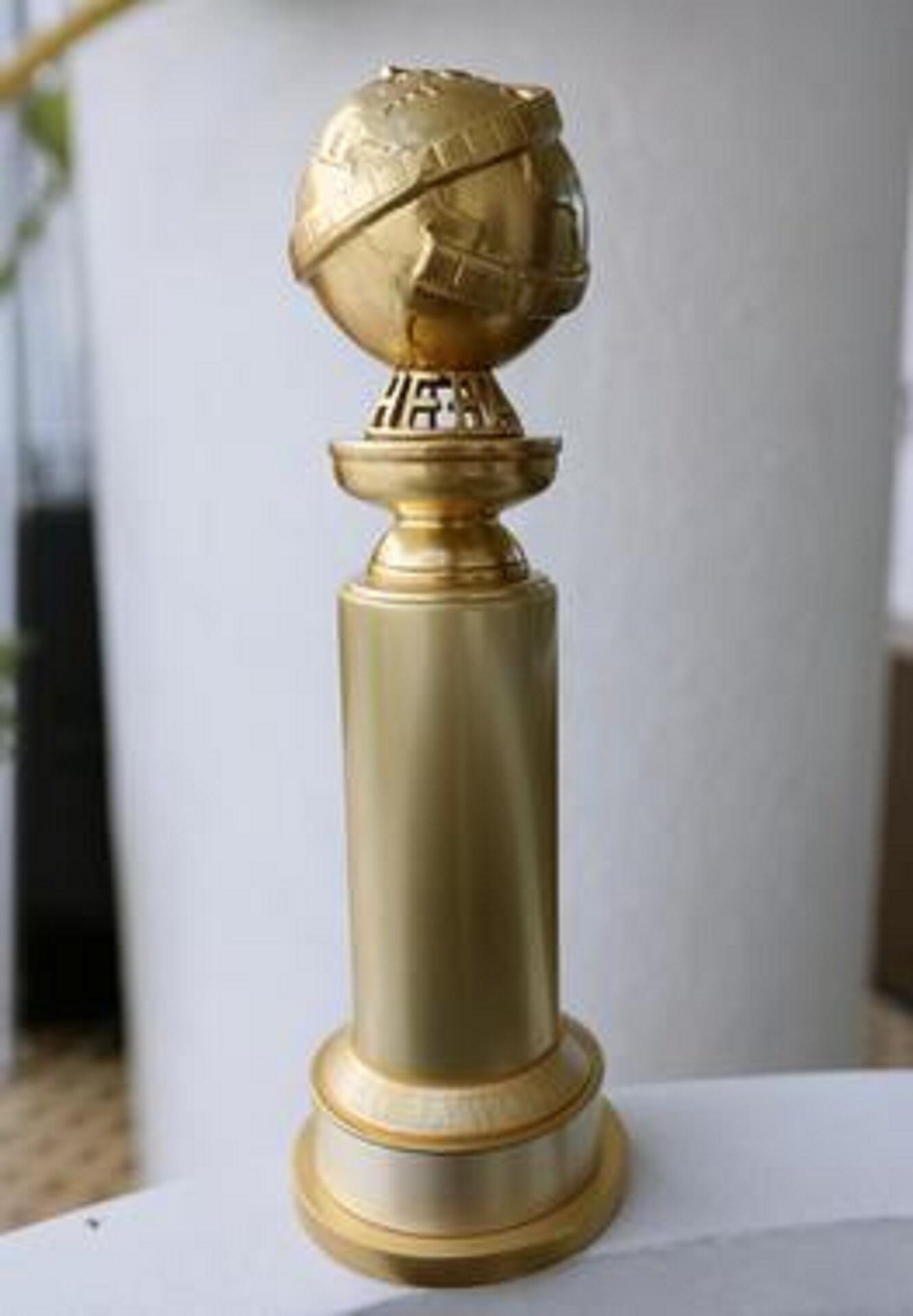 A golden statuette with a column body and a globe mounted atop it.