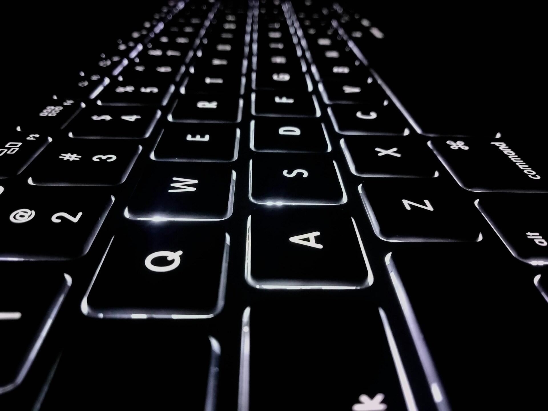 Close-up angled view of a black keyboard with illuminated white backlit keys.