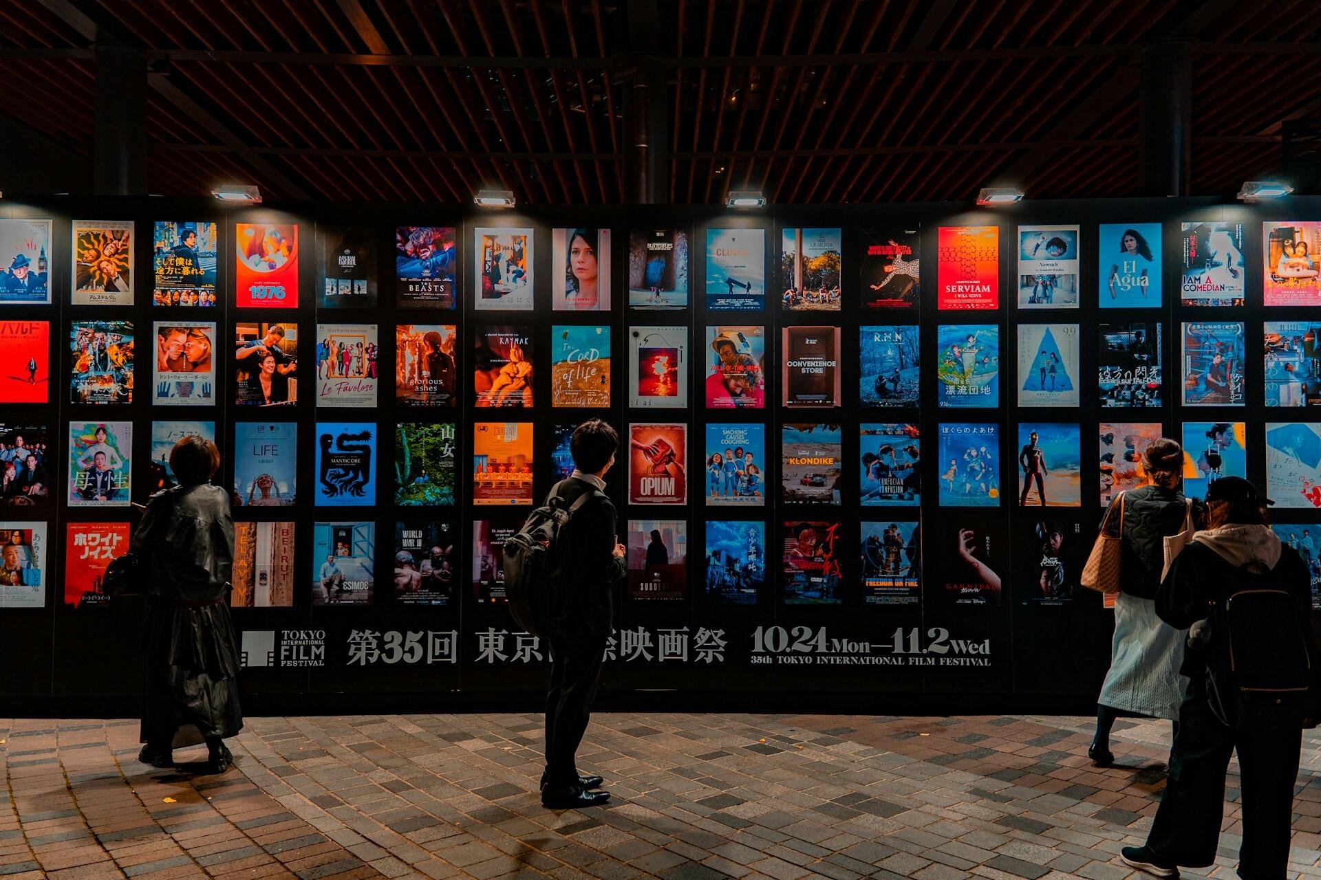 People standing in front of a wall of posters at night. 