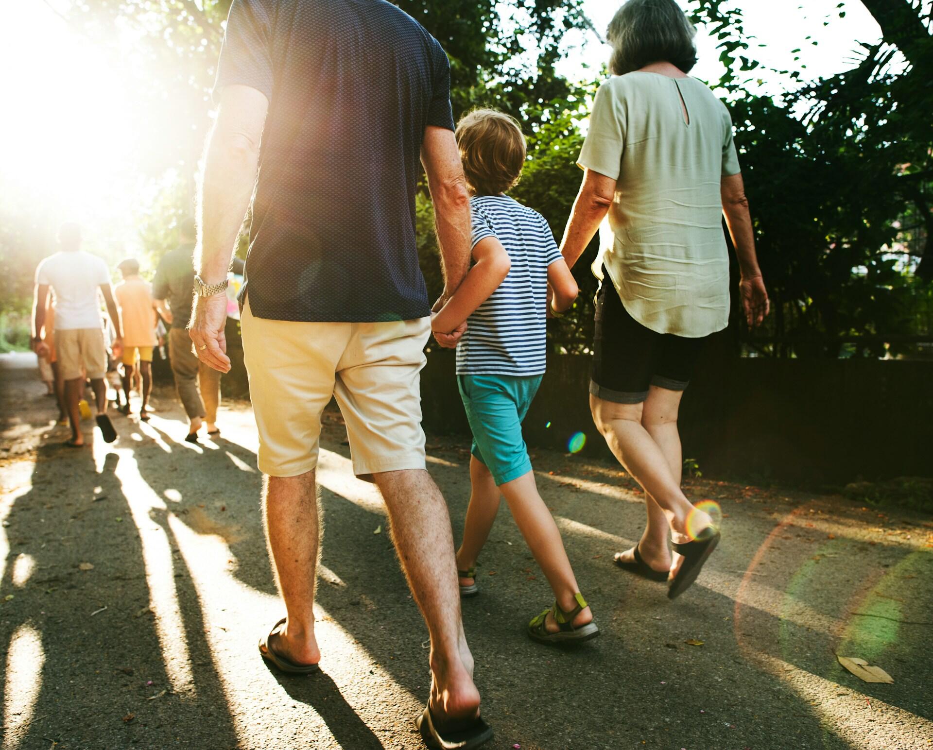 Two adults walk with a child between them on an outdoor path.