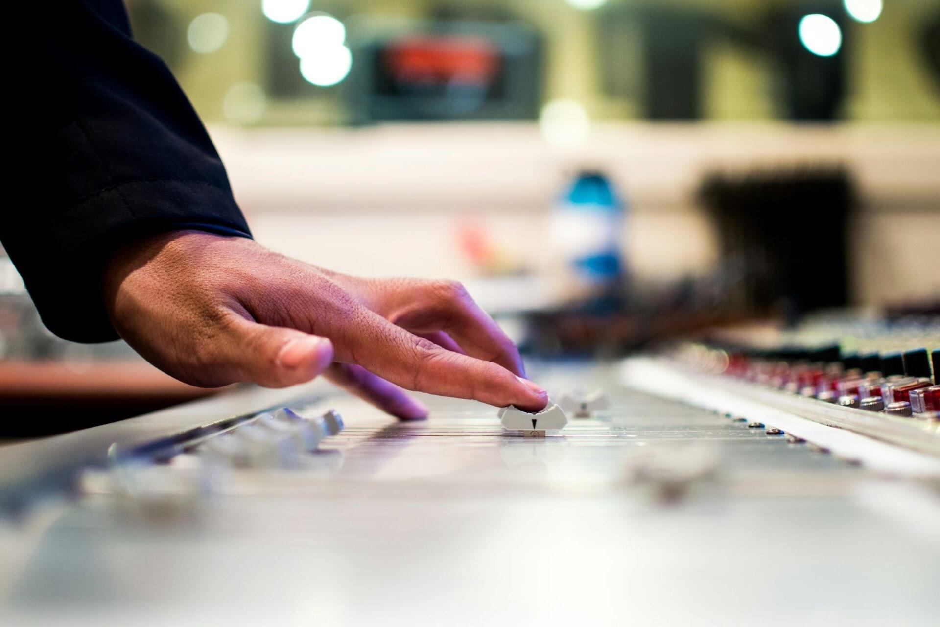 Hand adjusting slider on professional audio mixing console in recording studio