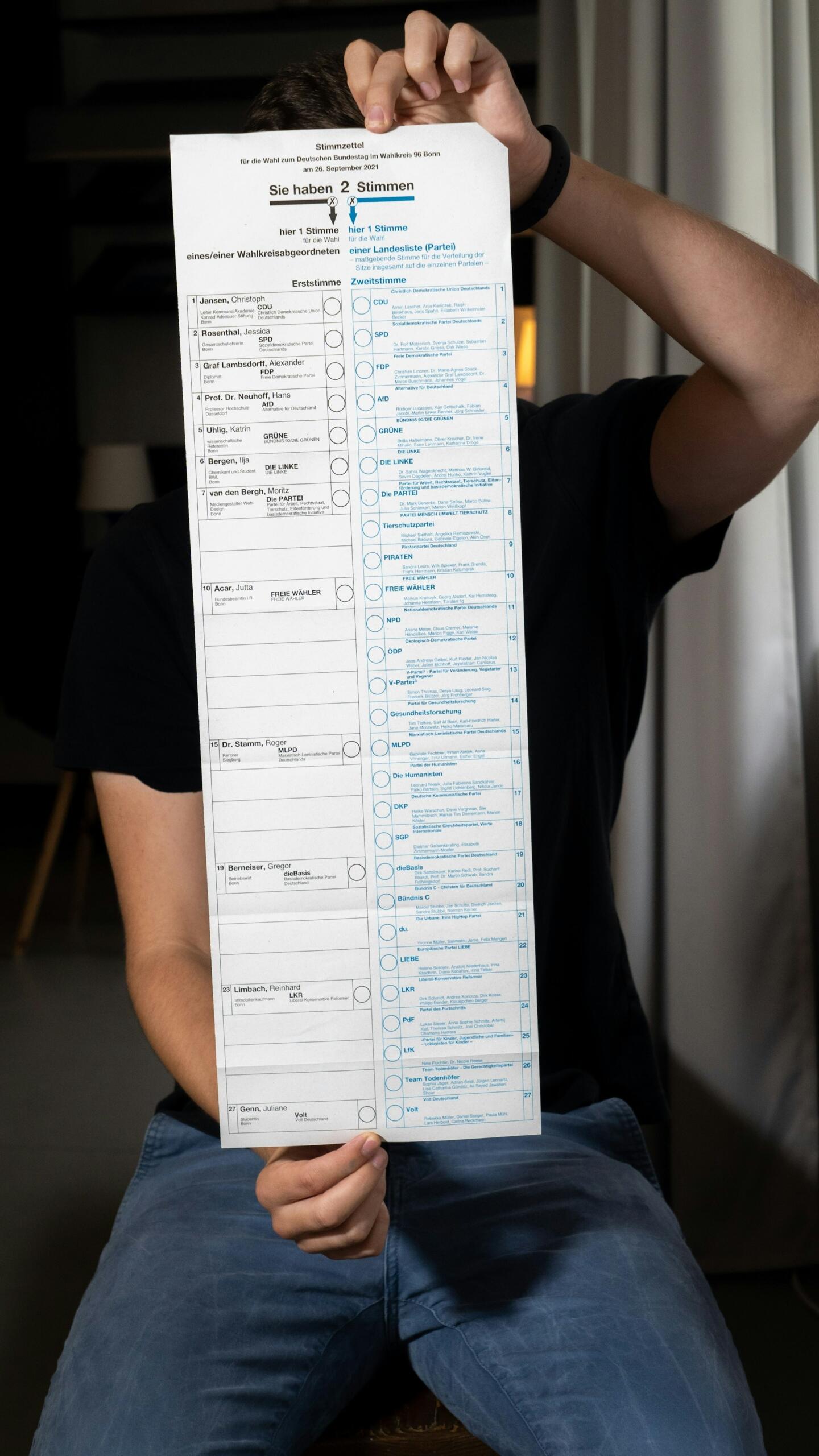 A person in a black tee-shirt holds up a longform ballot printed in blue and black ink.