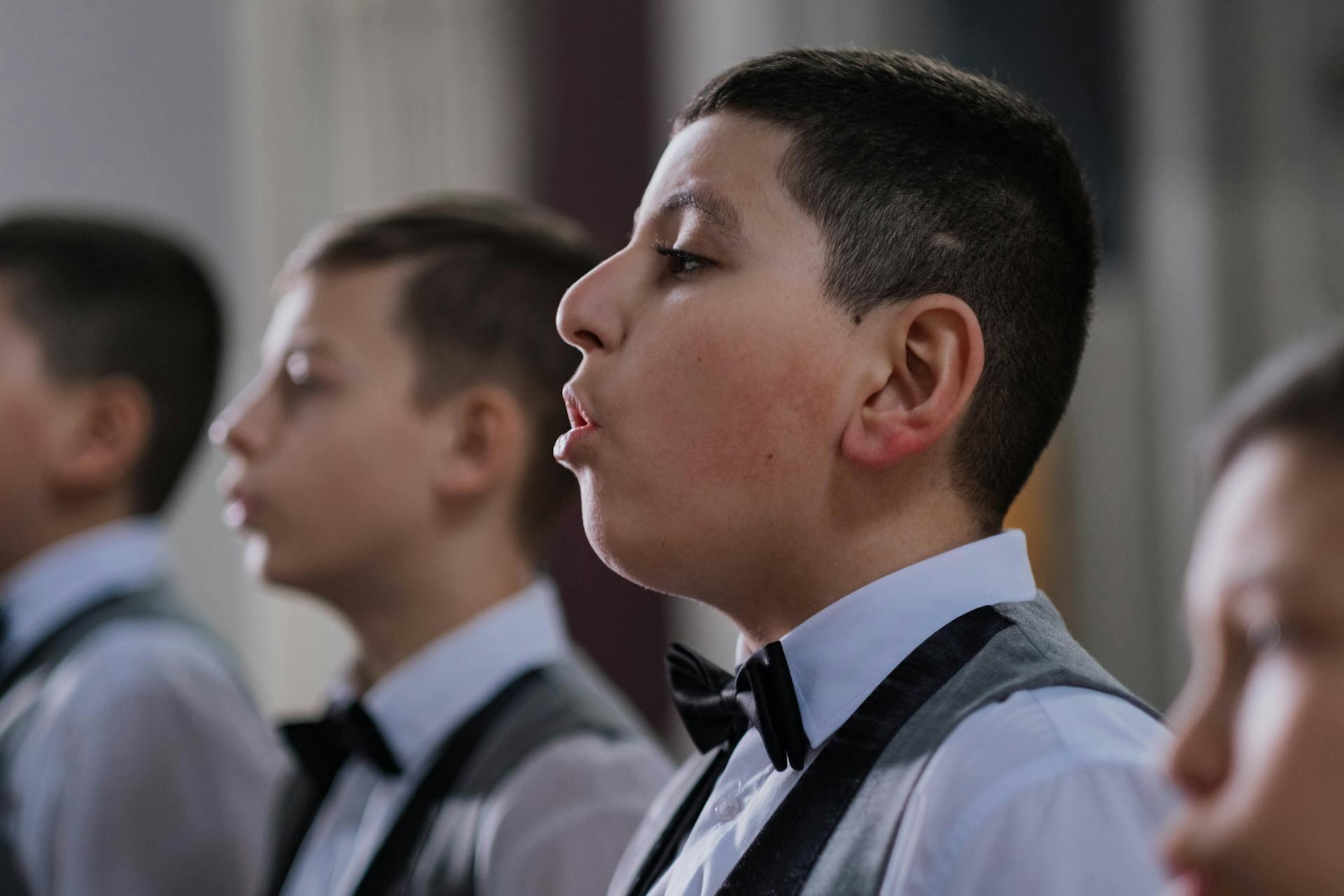 A group of boys in tuxedos, standing in a line, dressed formally with bow ties, focused and serious.