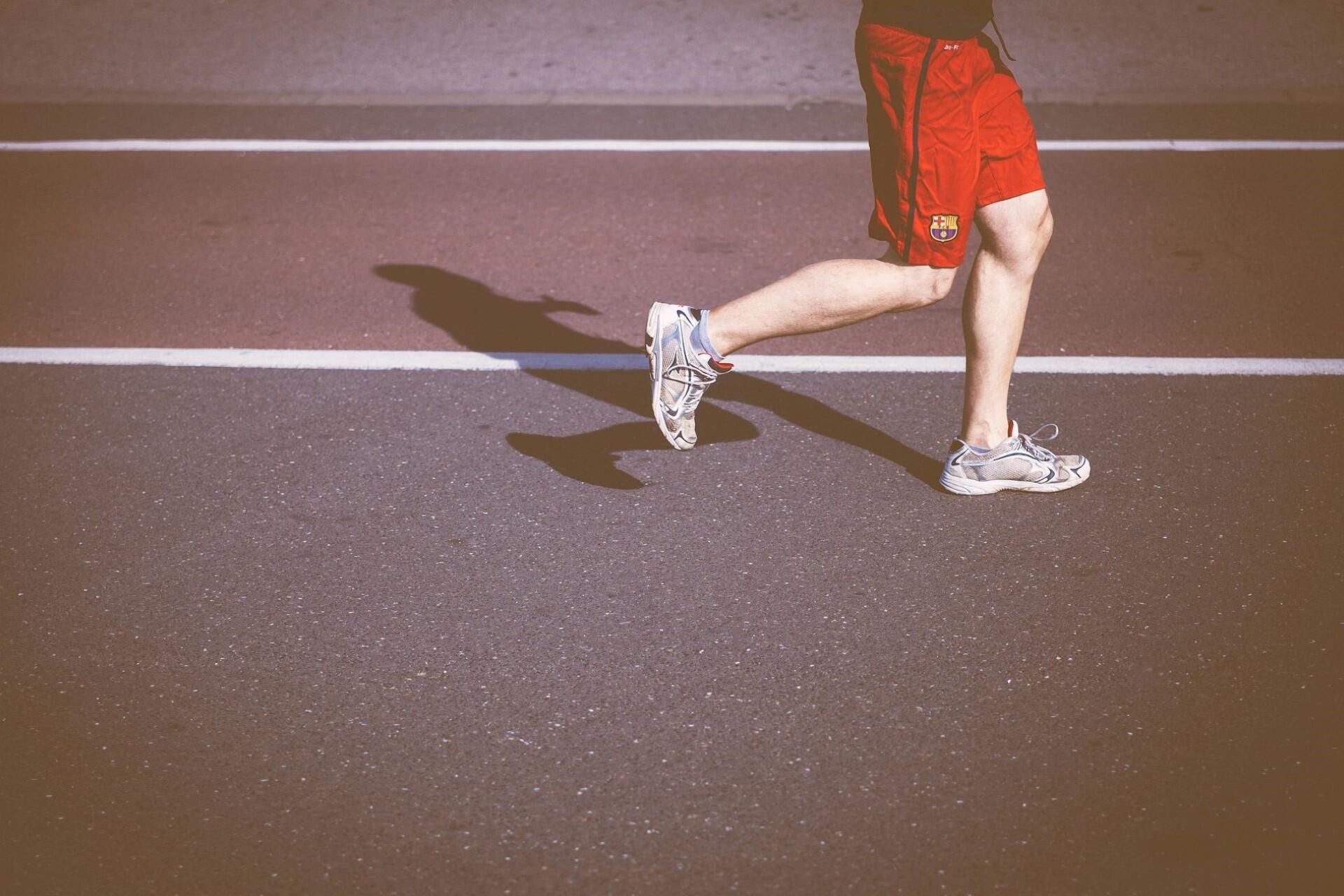 Runner wearing red shorts running on a road casting a shadow