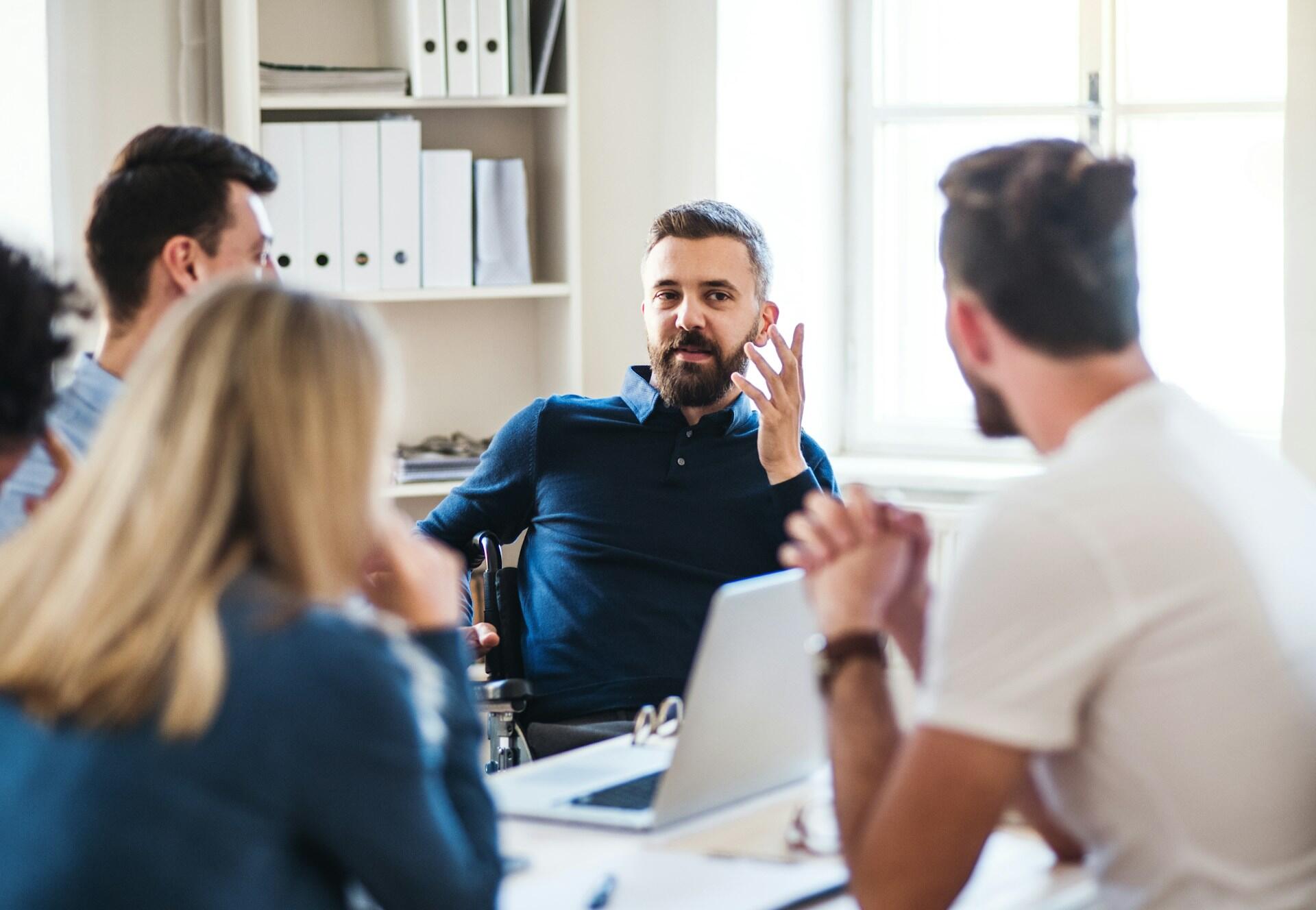Four people in business casual dress sitting around a table with a computer on it in an office.