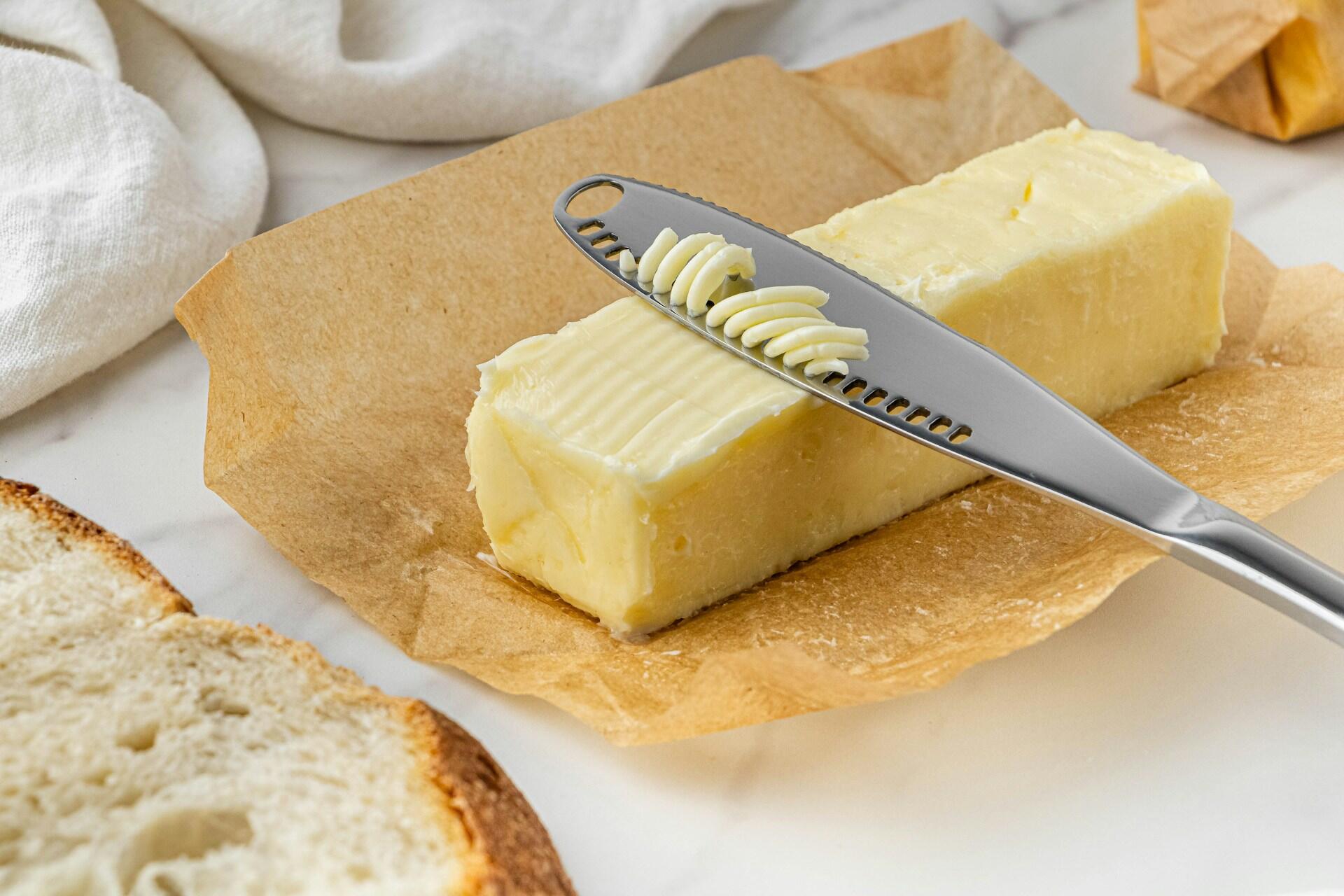 A stick of butter with a scraper pulling curled shavings from it.