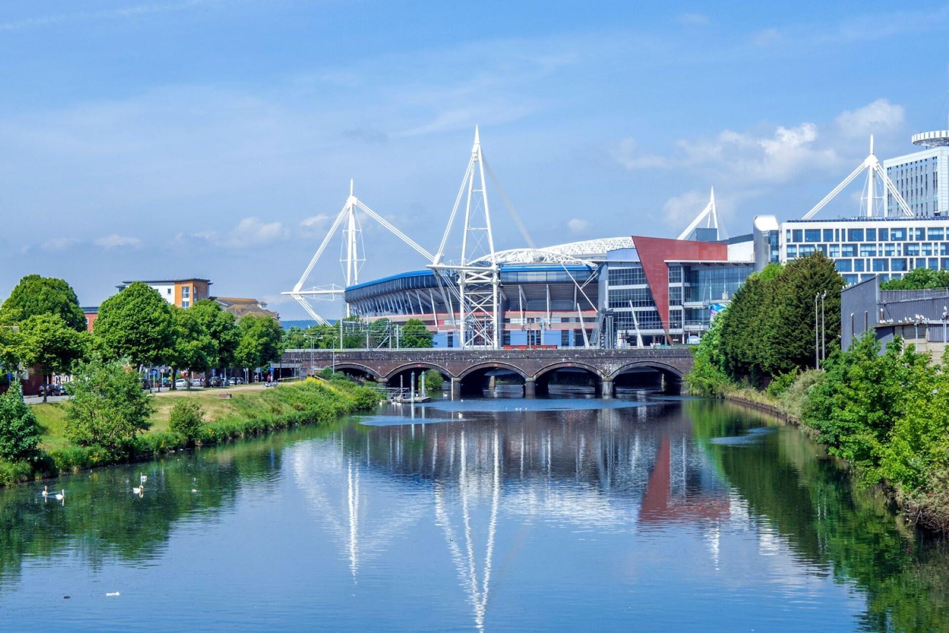 Millennium Stadium and Cardiff skyline reflected in the River Taff with a stone bridge in the foreground