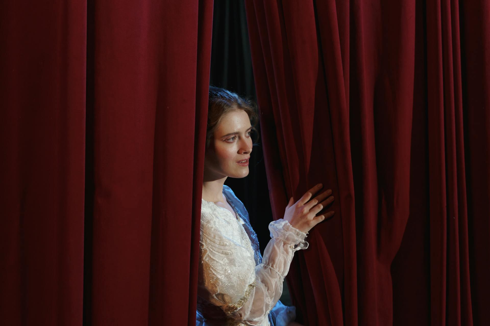 Lady in dress standing by red theatre curtain