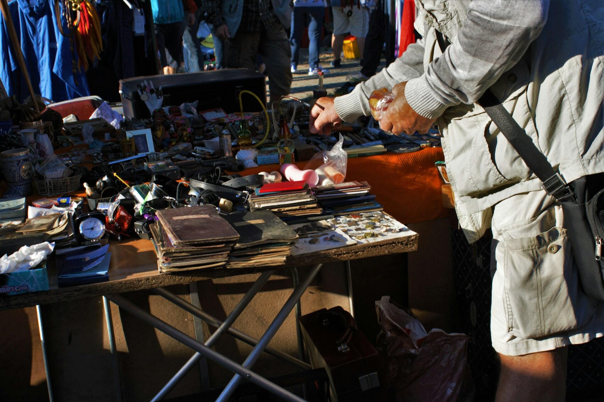 A person looking through wares for sale at an open market on a sunny day.