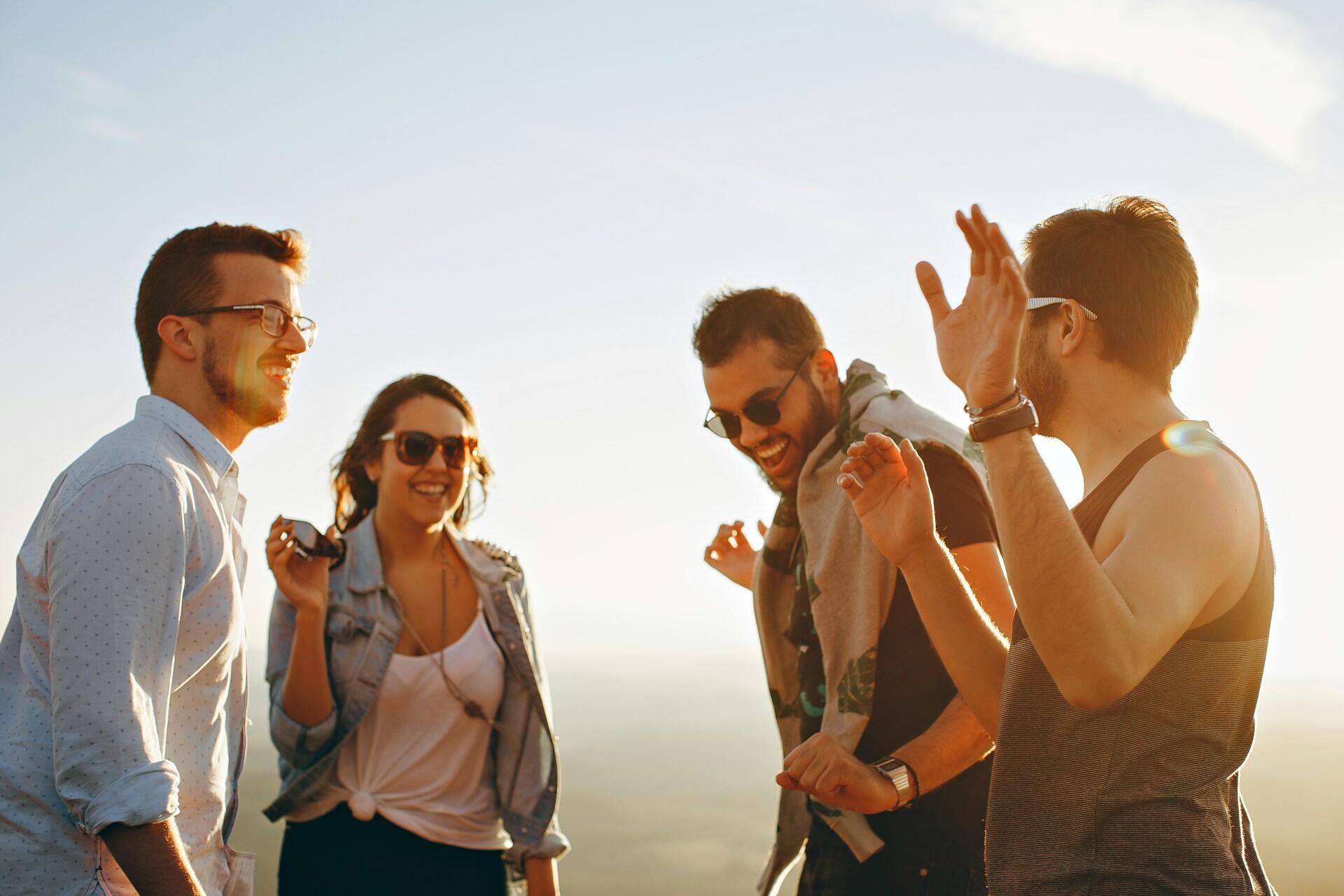 A group of four friends engages in lively conversation against a sunset backdrop, capturing a moment of joy and connection.