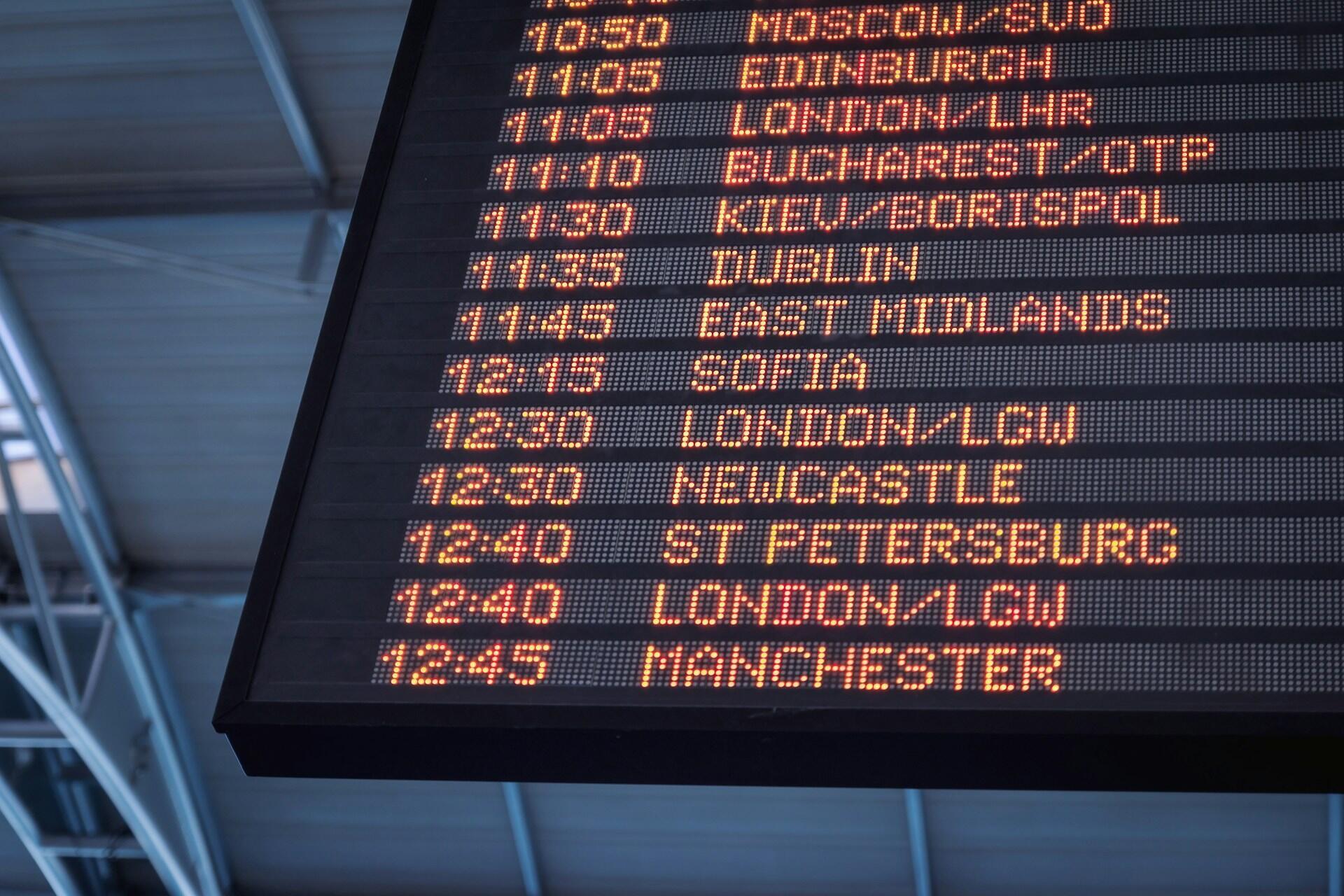 A digital airport schedule board showing times and city names in orange lights.