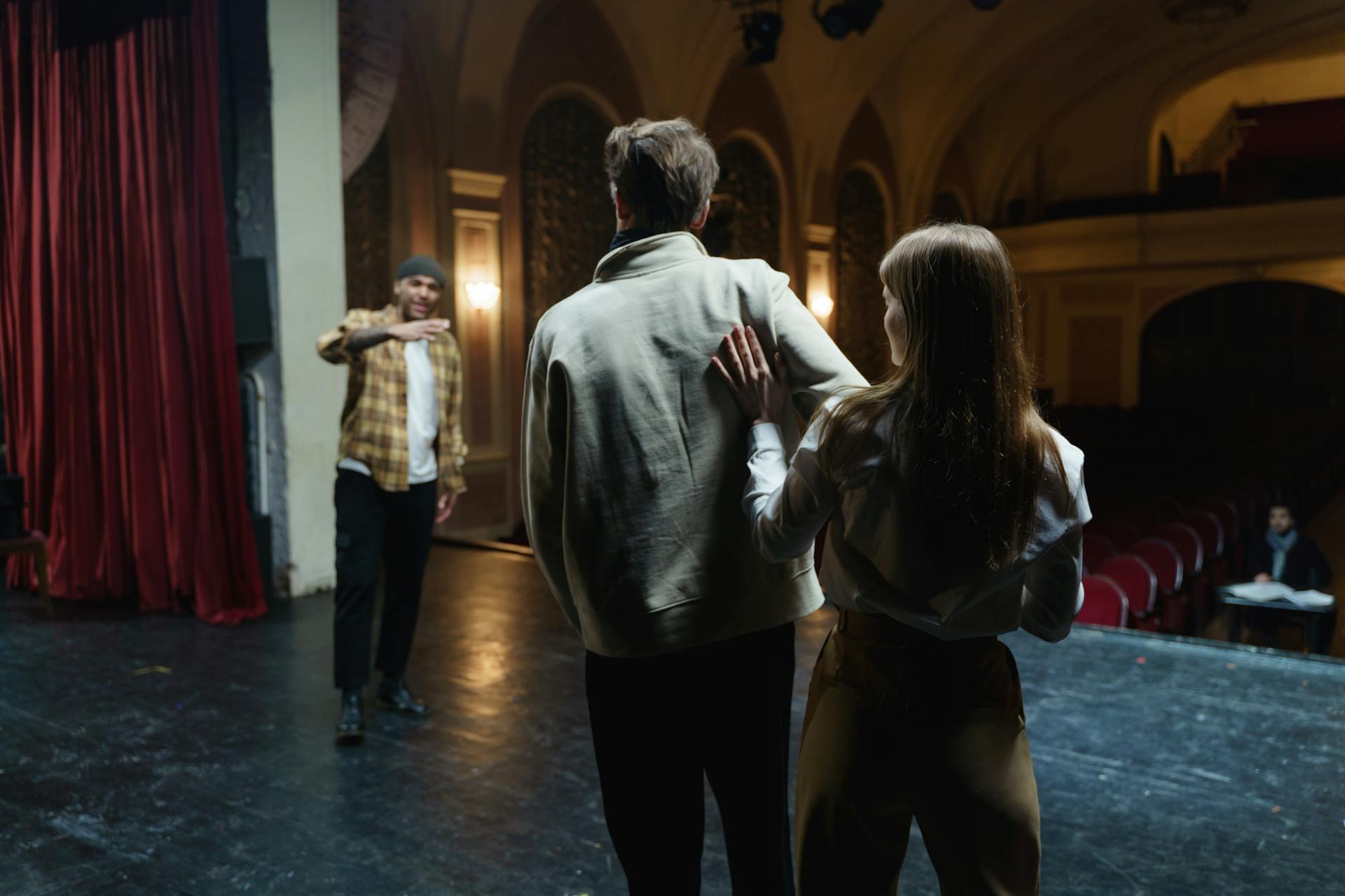 Two stage actors listening to a man talking to them on stage