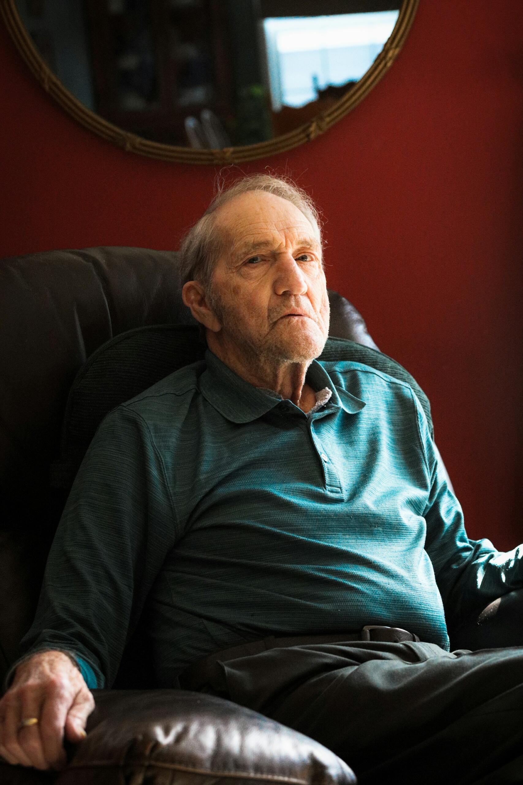 An older man in a green shirt seated in an armchair in a red room. 