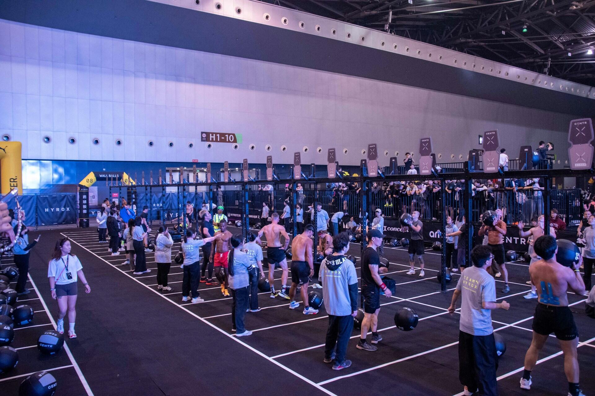 Athletes performing wall ball exercises inside an indoor competition venue with judges and spectators nearby