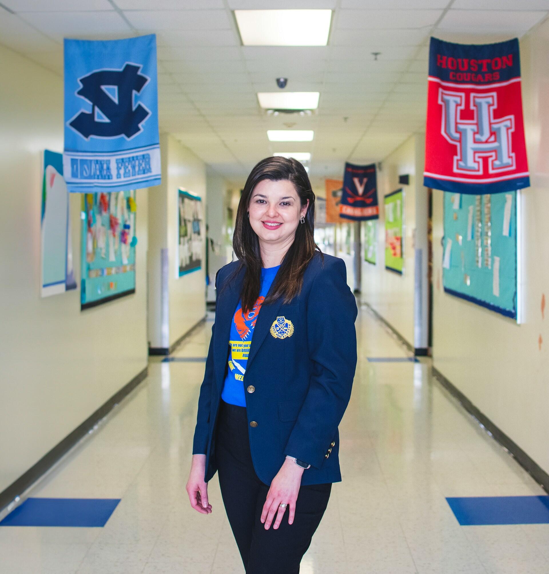 A person in a blue blazer stands in a school highway adorned with pennants and banners.
