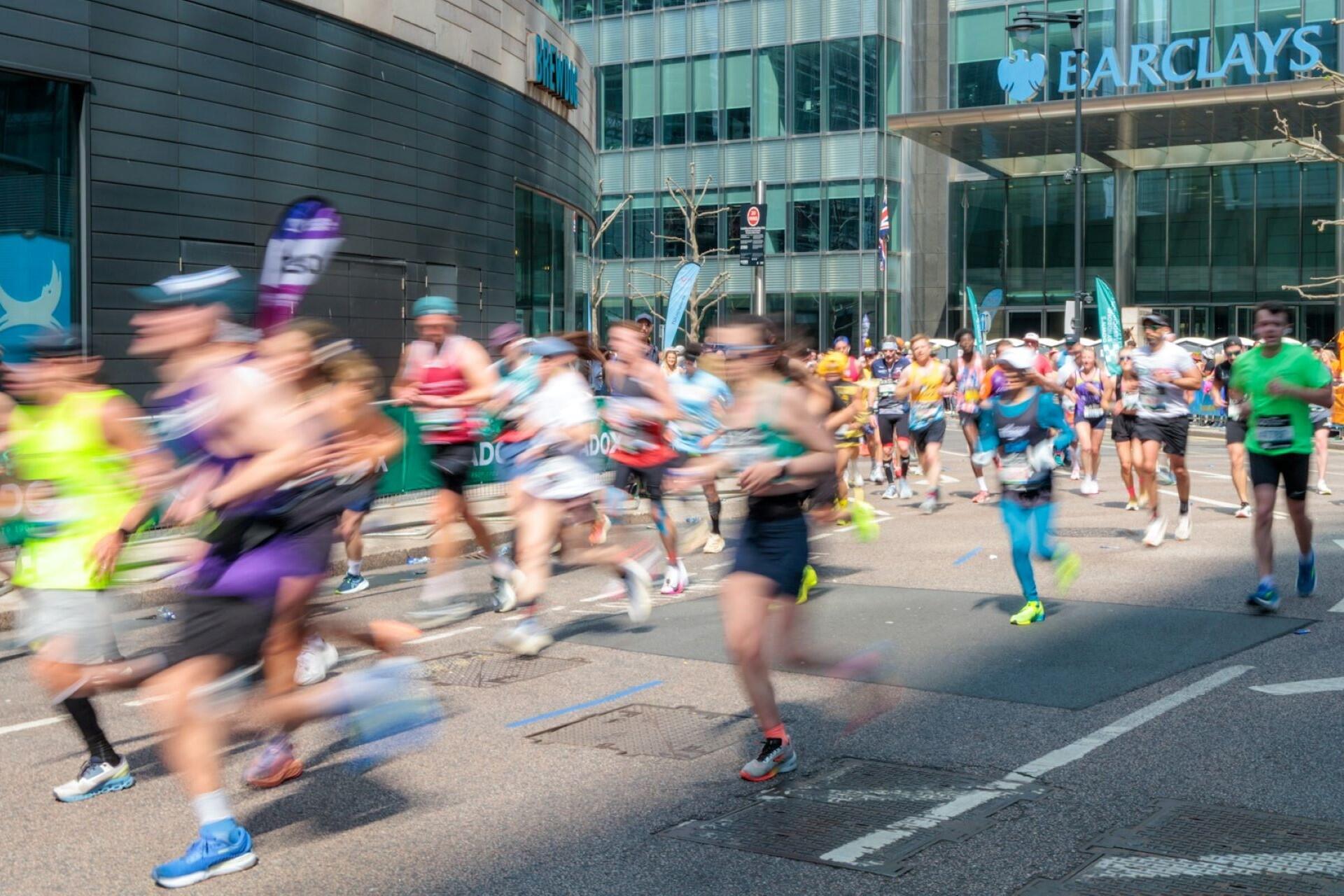 Group of marathon runners racing through a city street past modern buildings during a road marathon.