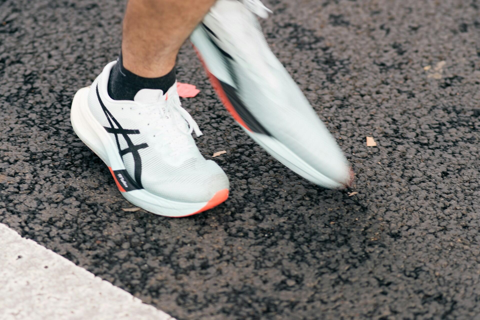Close up of runner wearing white running shoes stepping on asphalt road