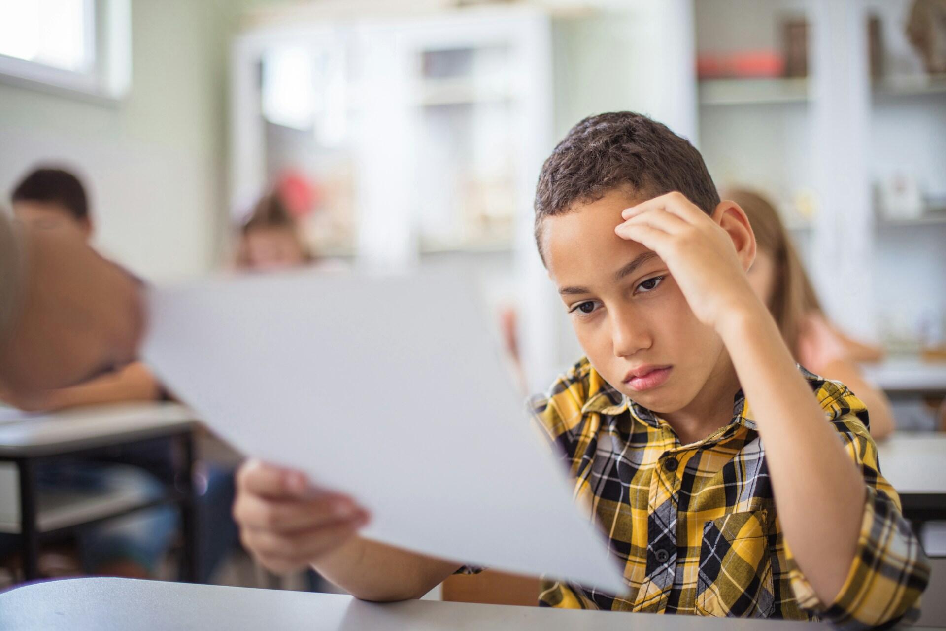 A child in class looks dismayed over the paper the teacher is handing him.