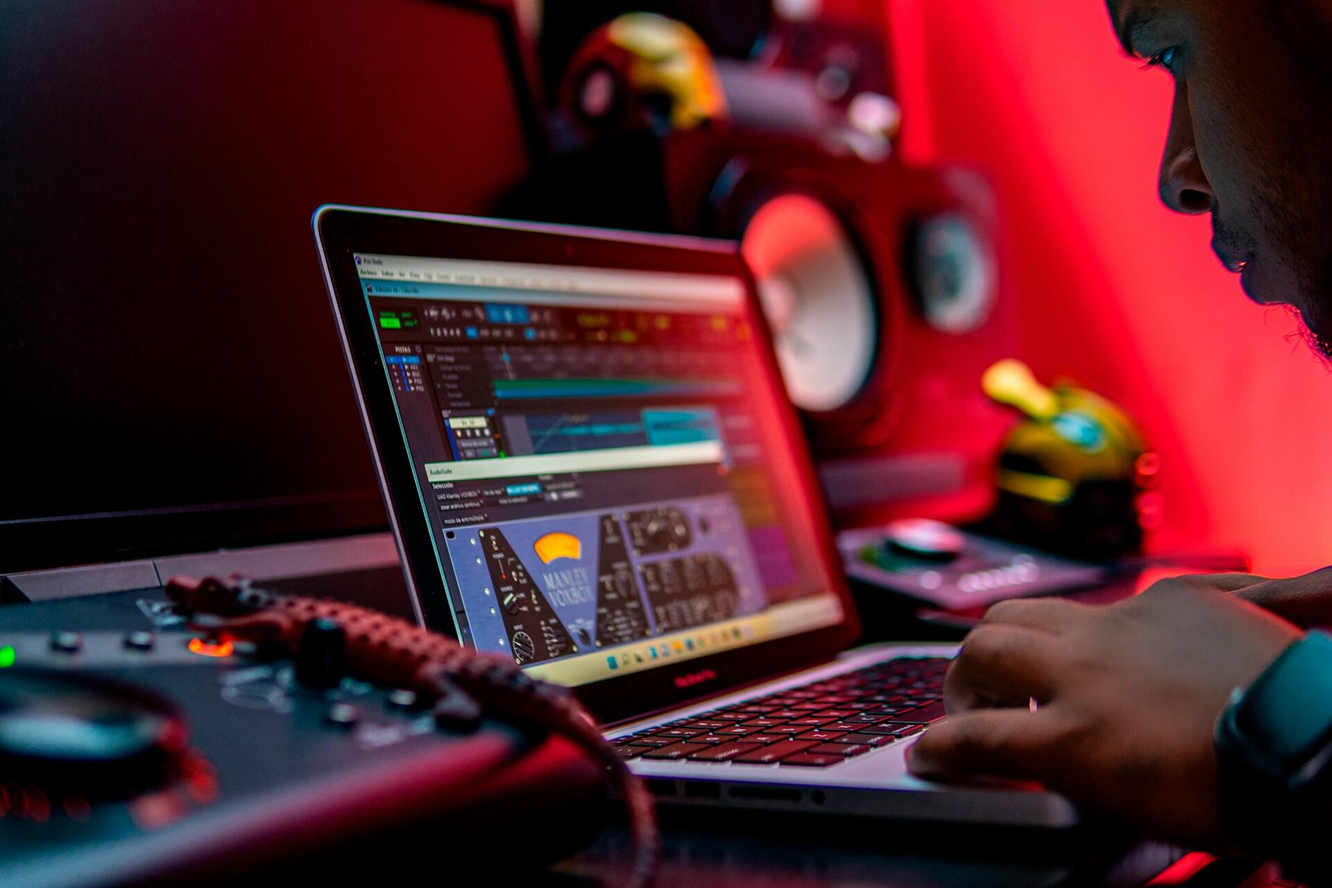 music producer working on laptop with audio plugins and studio monitors