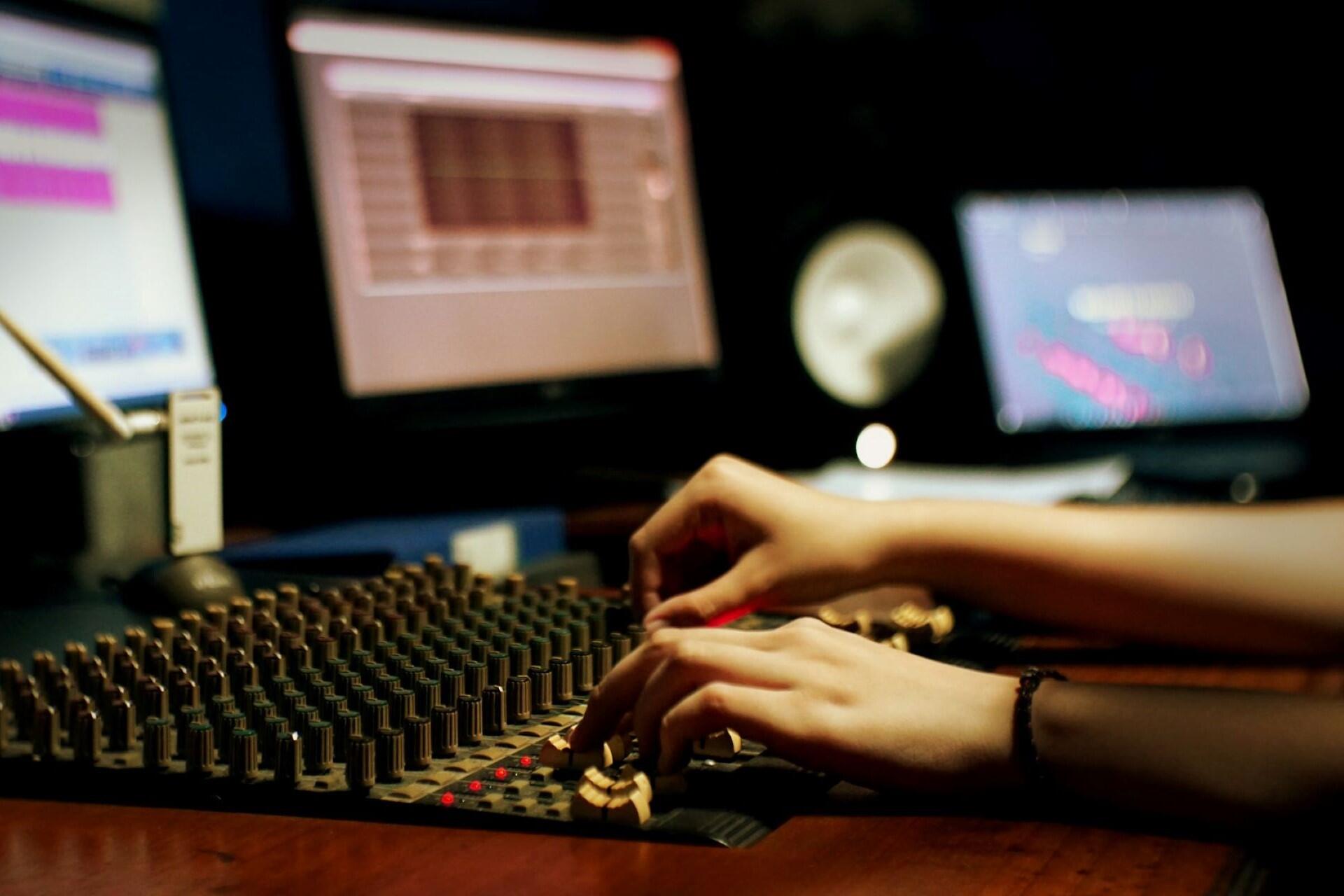 Student working on audio mixing console with digital audio workstation screens in recording studio