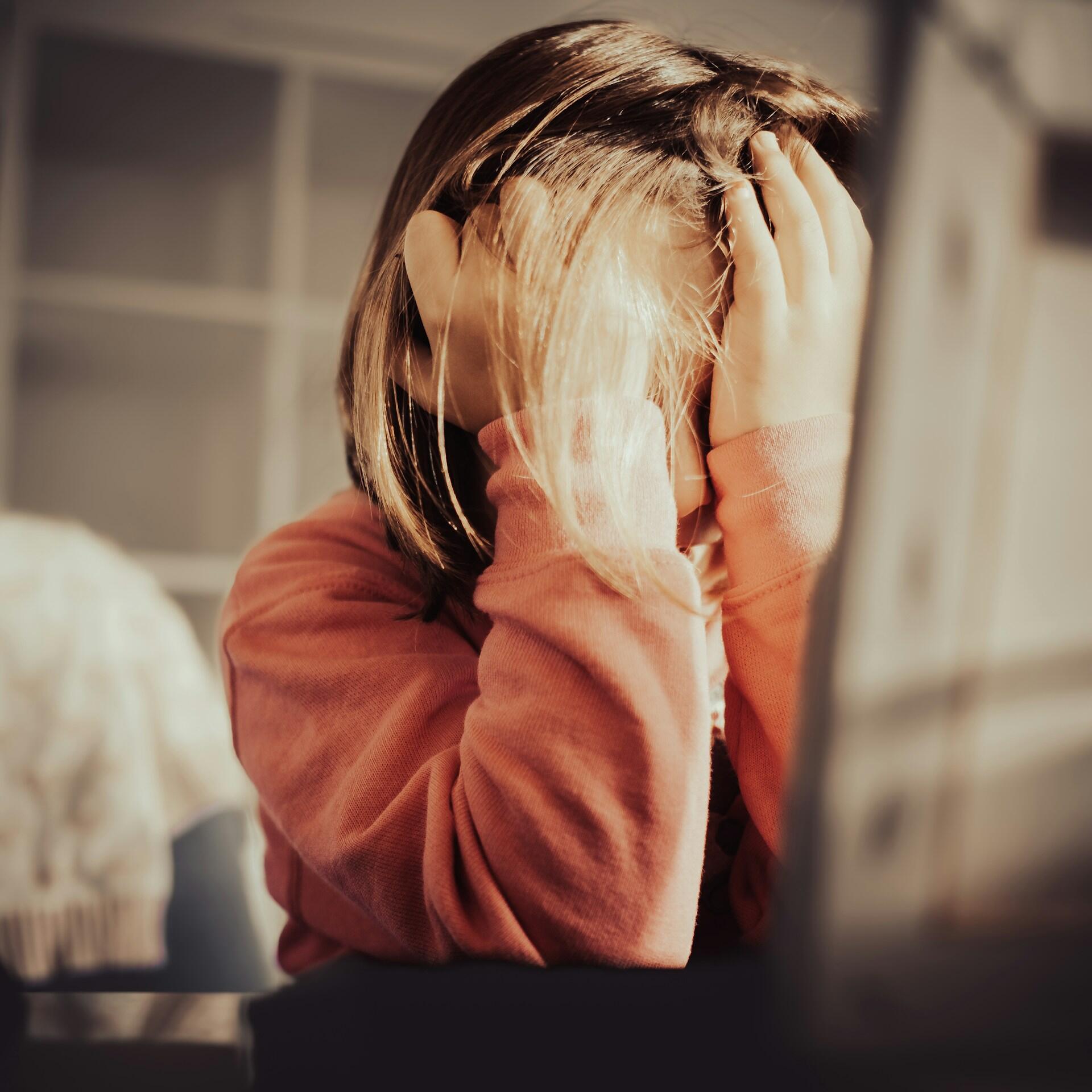 A person holds their hands over their face while raking their fingers through their hair.