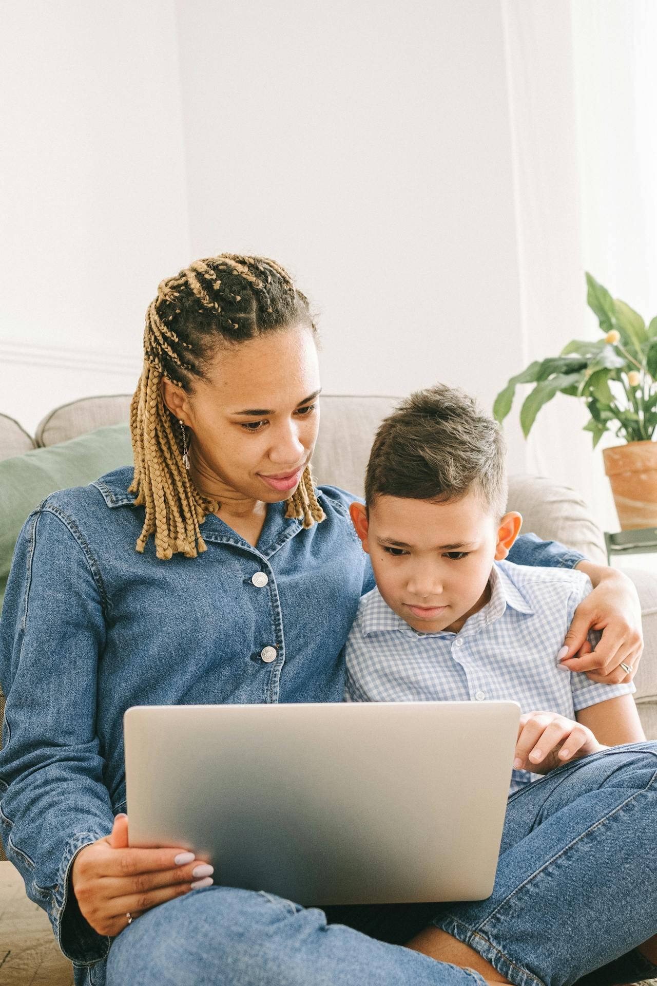 A person in denim attire and a child sit together on a couch, engaging with a laptop, surrounded by indoor plants.