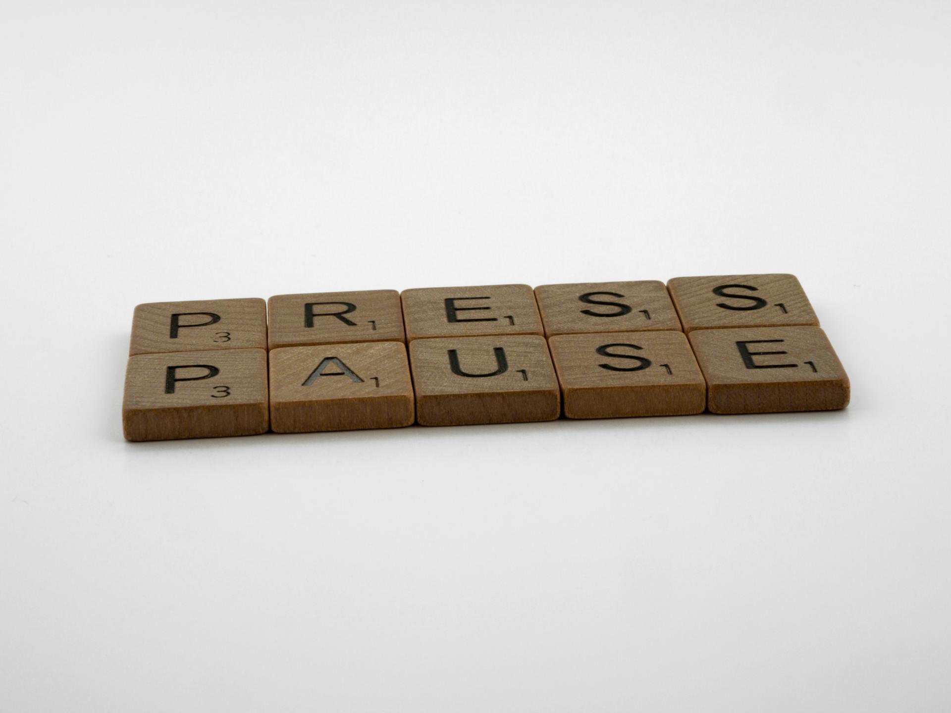 Image of scrabble pieces placed on a white background that spell out press pause
