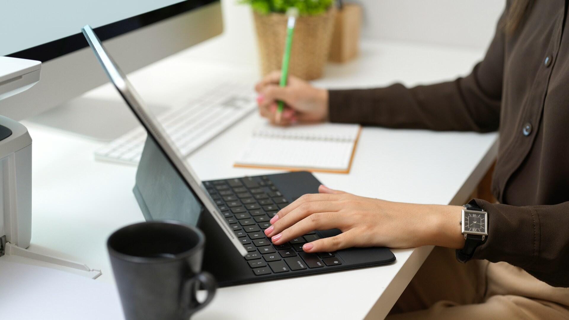 A person working a computer while writing in a notebook.