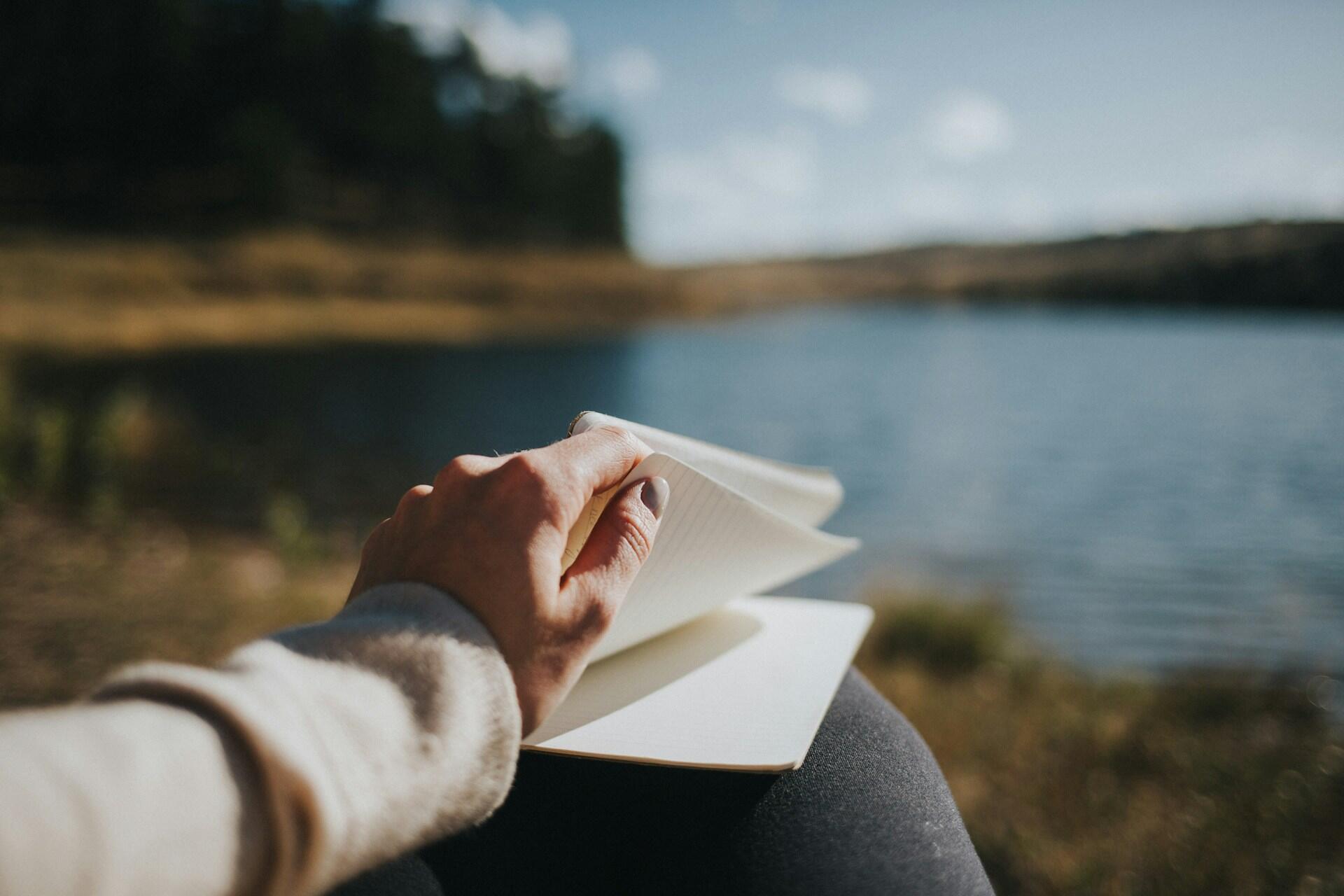 person holding notebook by a lake reading or writing
