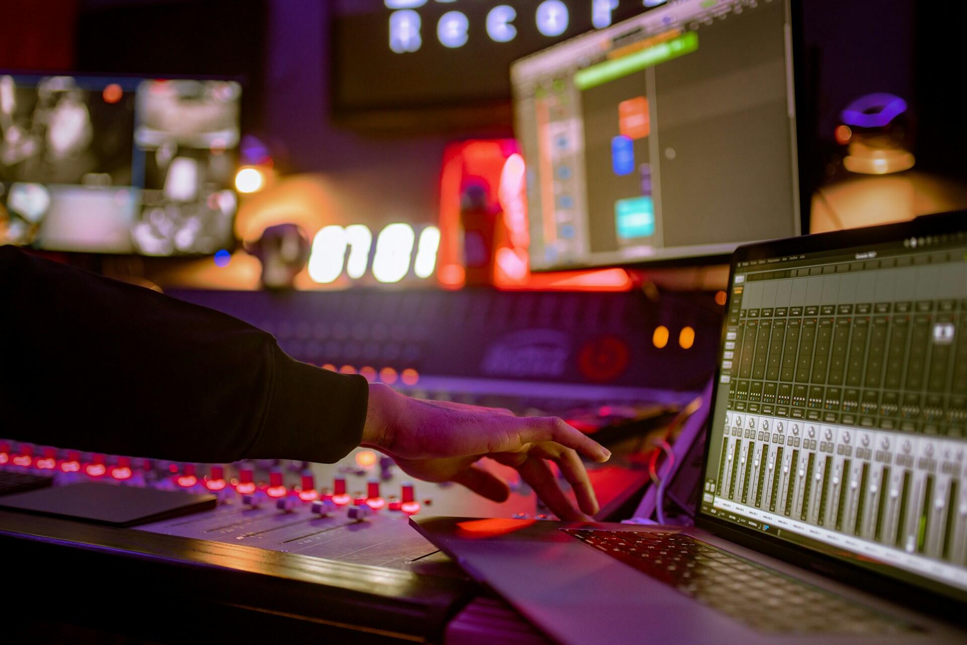 Music producer adjusting controls on a mixing console in a professional recording studio.