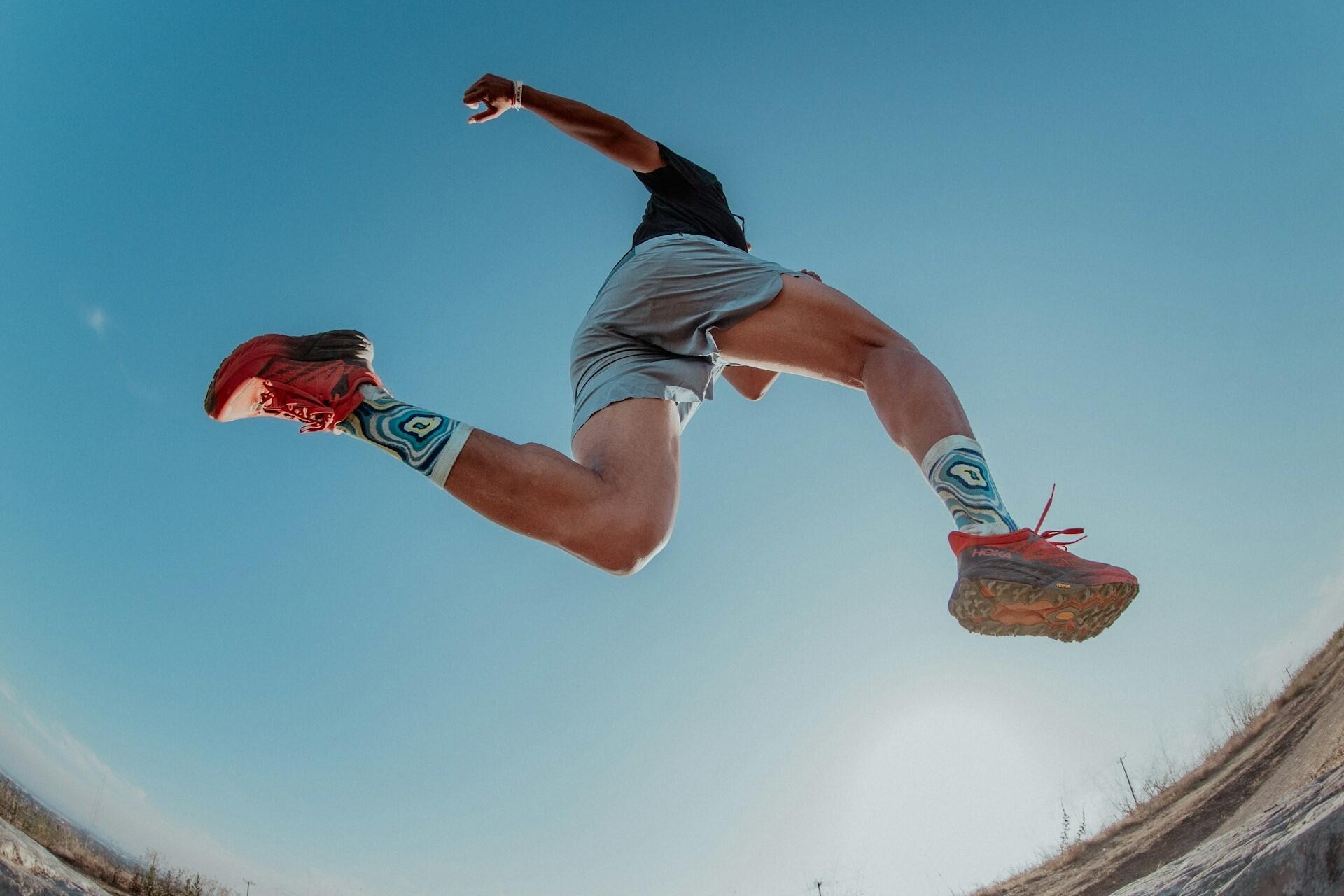 Low angle view of a runner mid stride wearing red running shoes against a blue sky.
