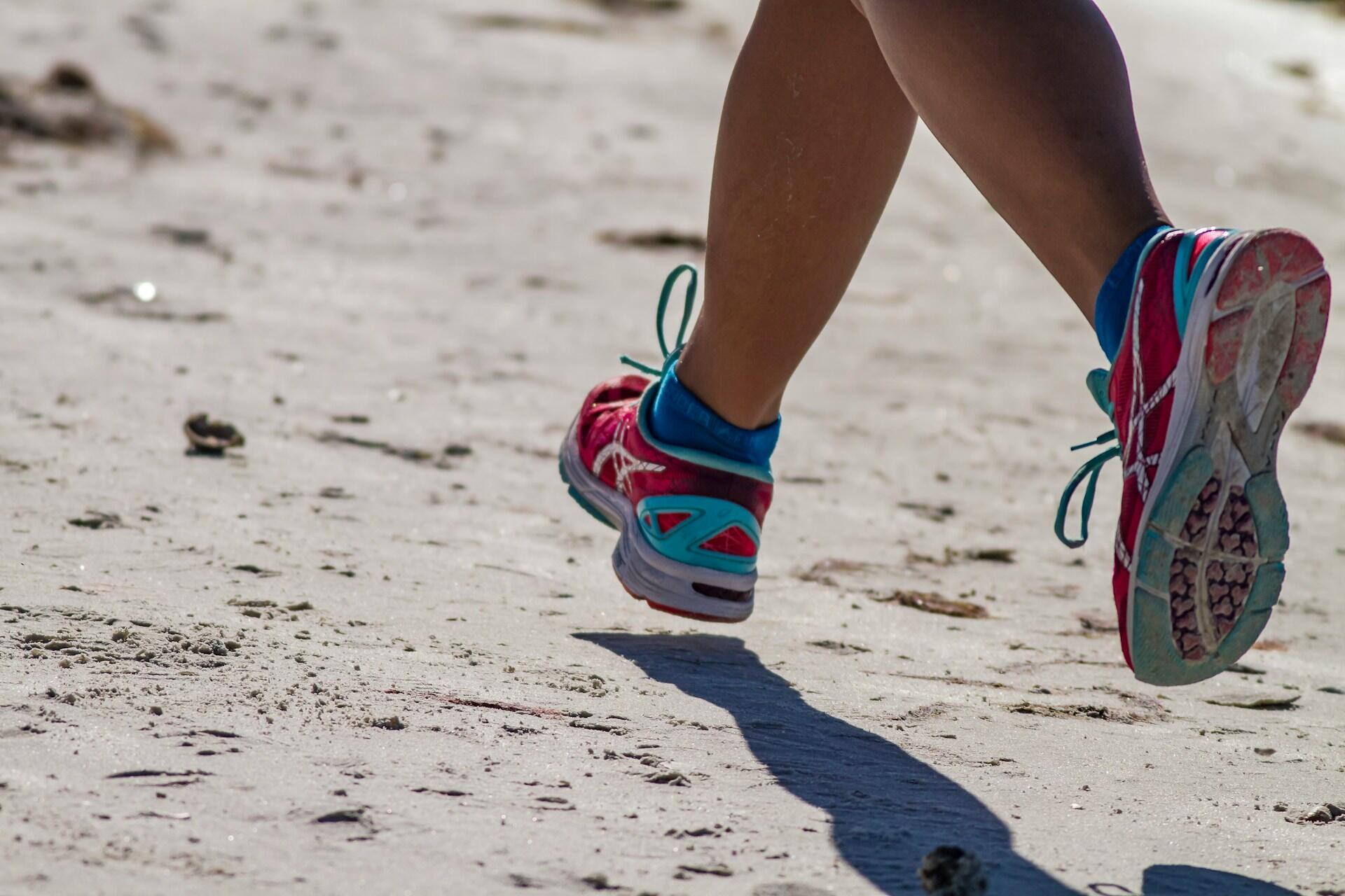 Close up of a runner’s legs and running shoes jogging along a sandy beach
