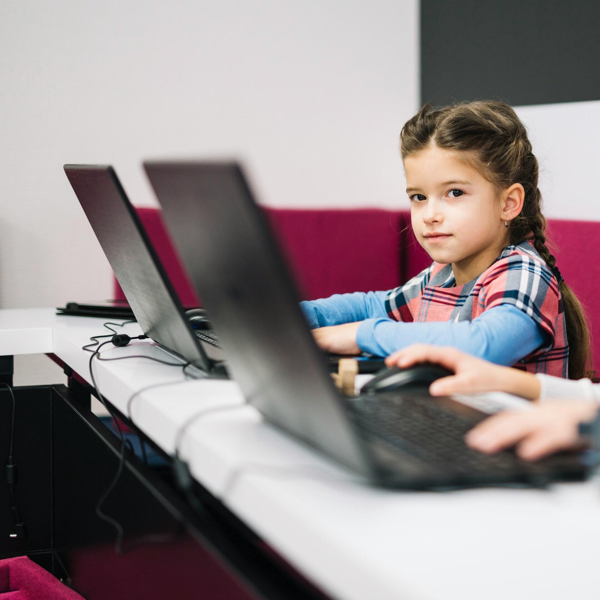 A student sits at a white table with an open laptop computer in front of her. 