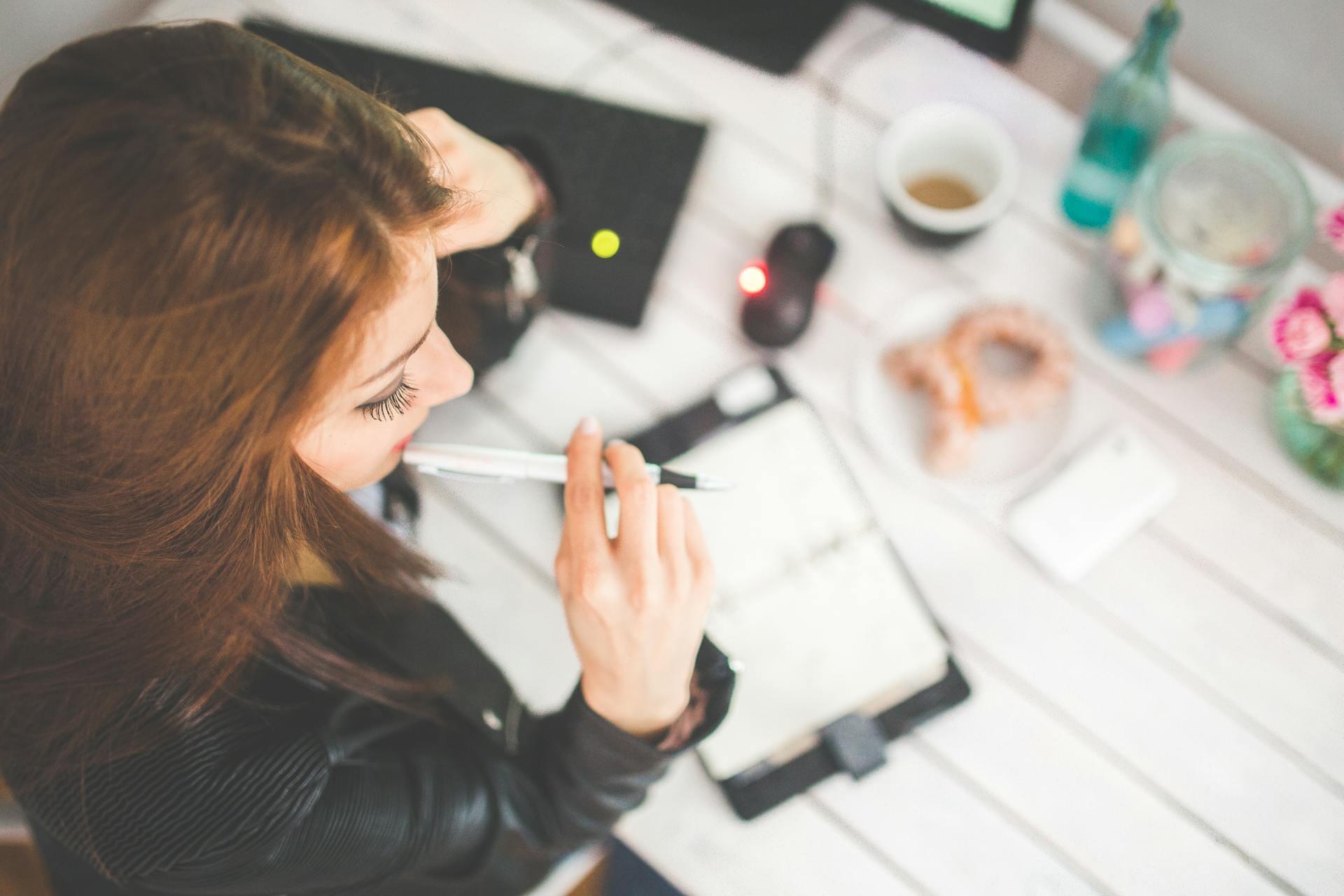 Woman sat at desk with pen in her mouth