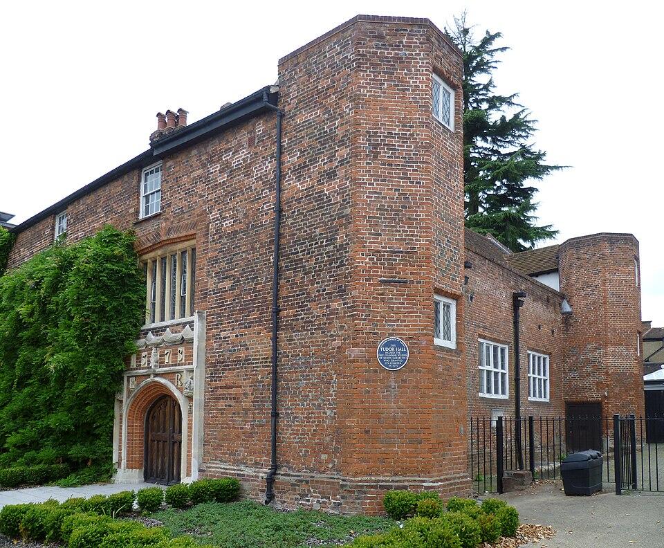 Historic Tudor Hall, a brick building with a prominent archway entrance, surrounded by greenery and tall trees.