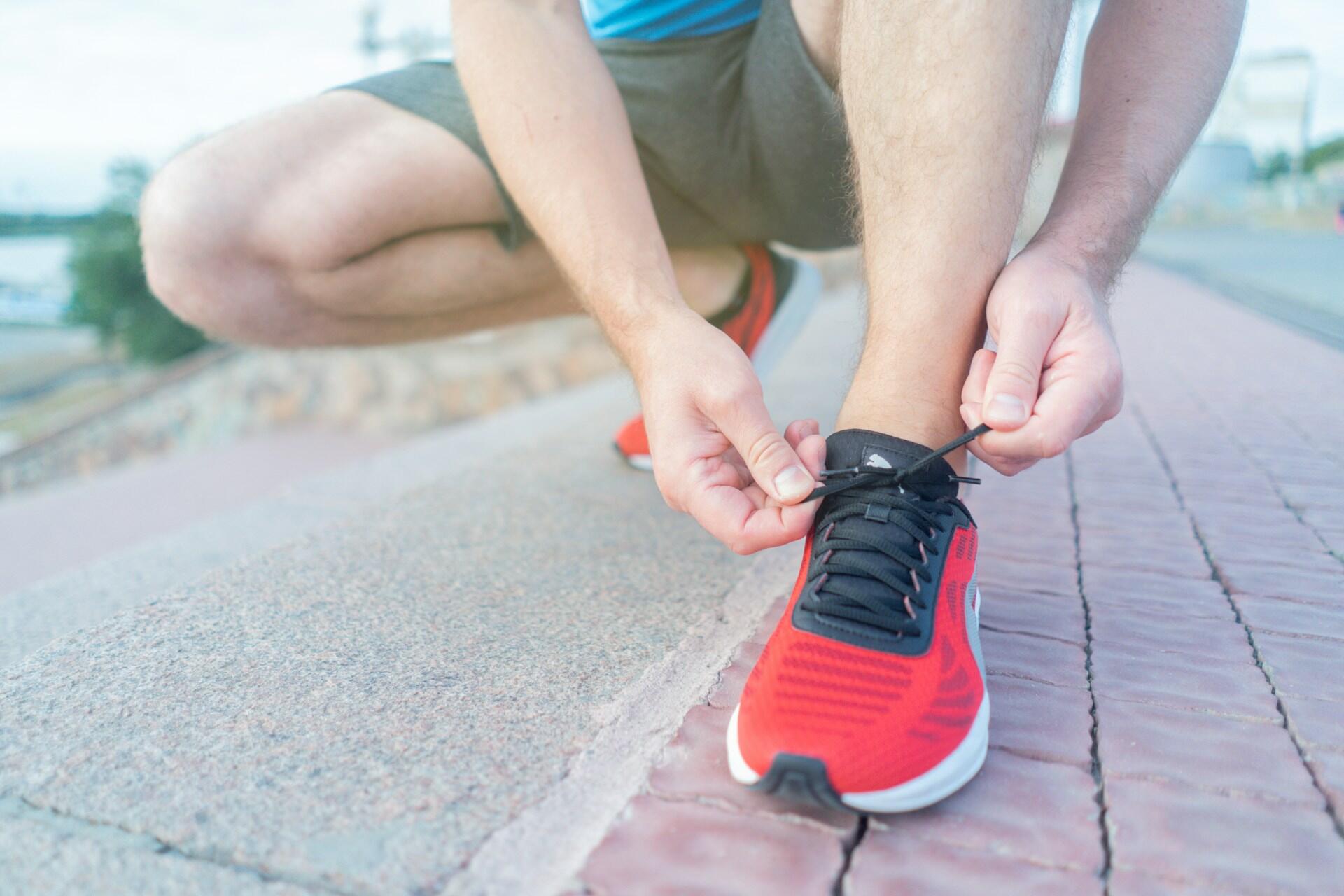 Close up of a runner tying the laces of red running shoes while crouching on a pavement.