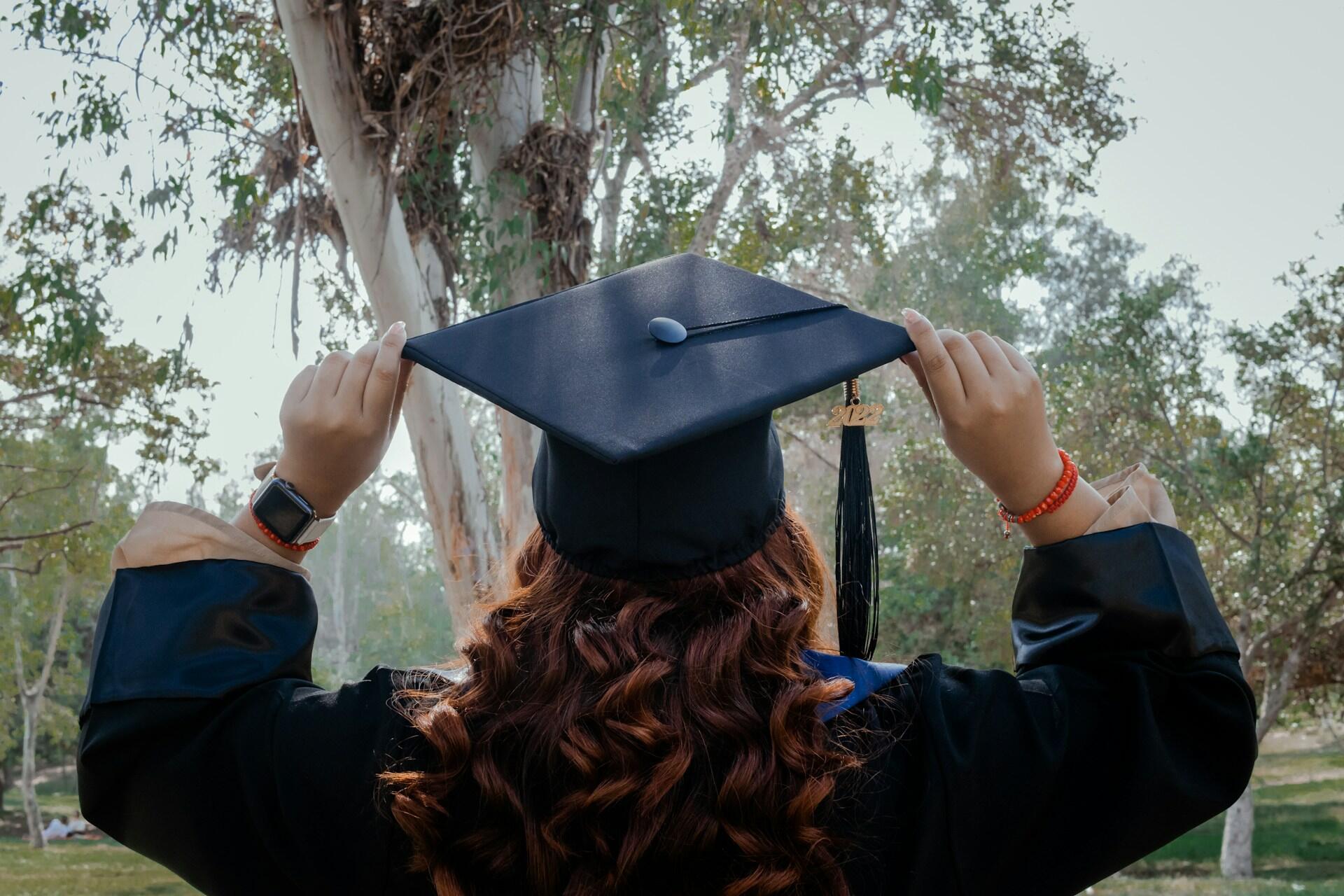 University graduate adjusting graduation cap outdoors after completing degree