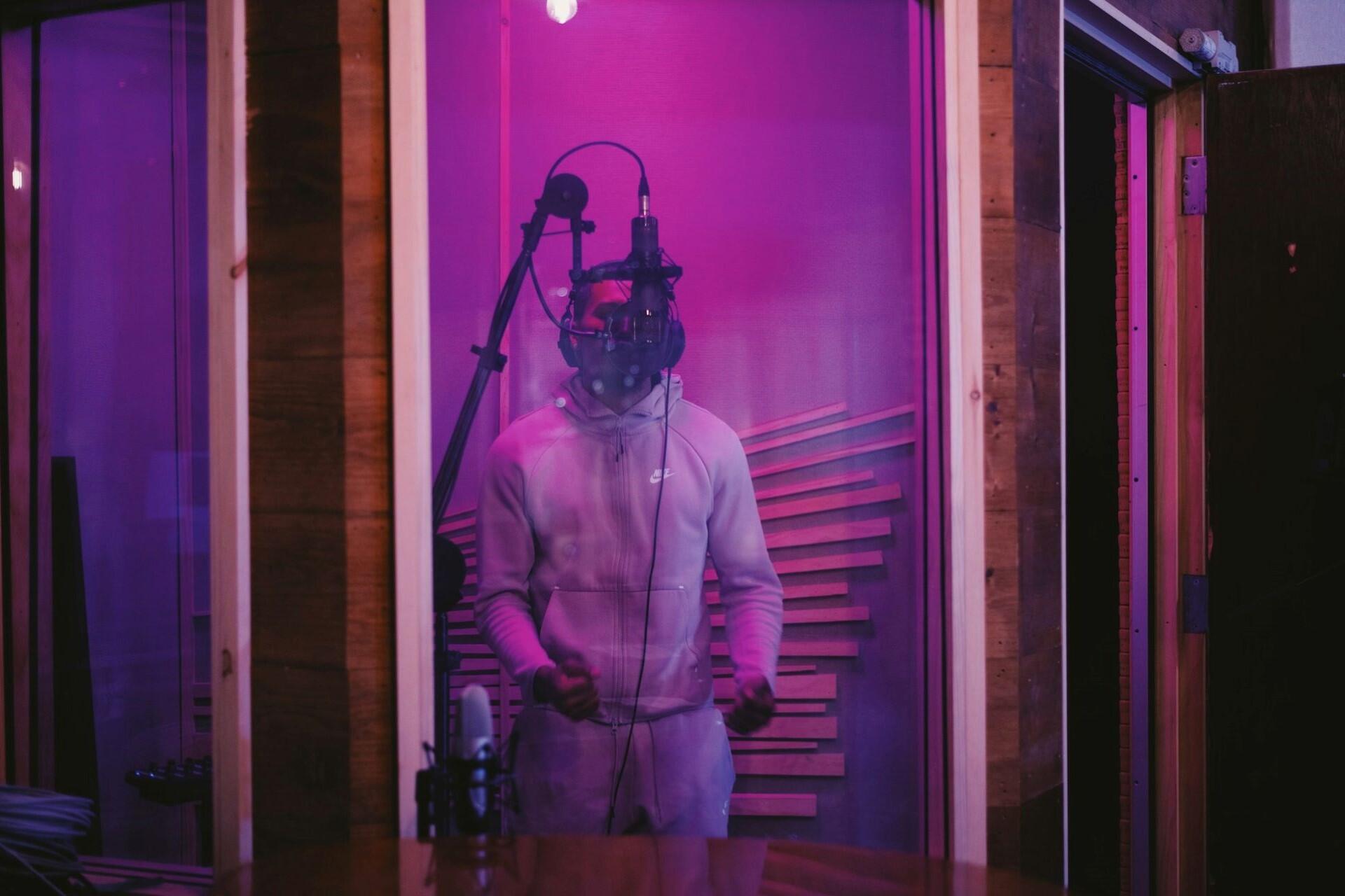 Music artist recording vocals in a professional studio vocal booth using a condenser microphone