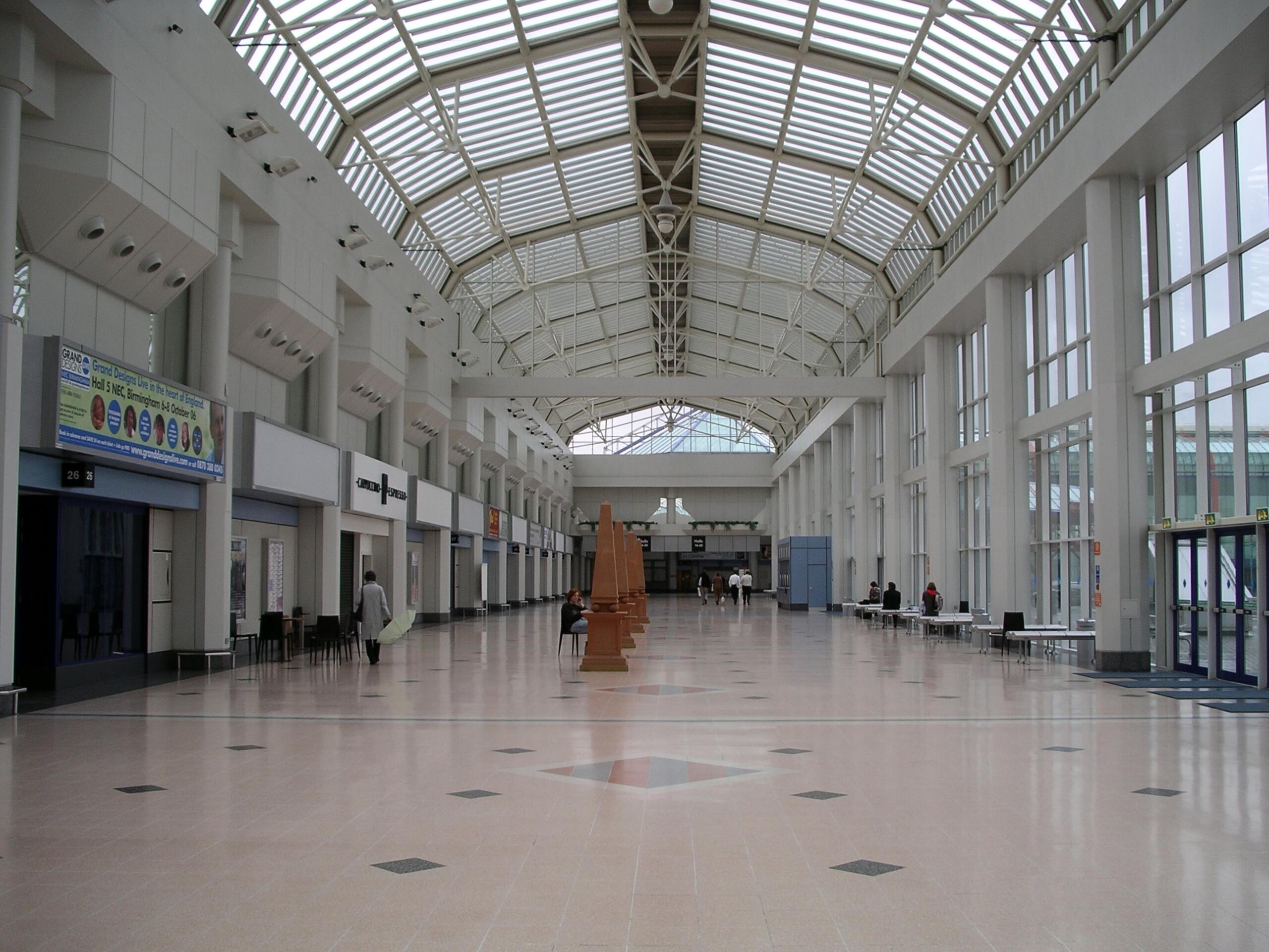 A wide hallway with a glass ceiling and wooden statues in the middle. 