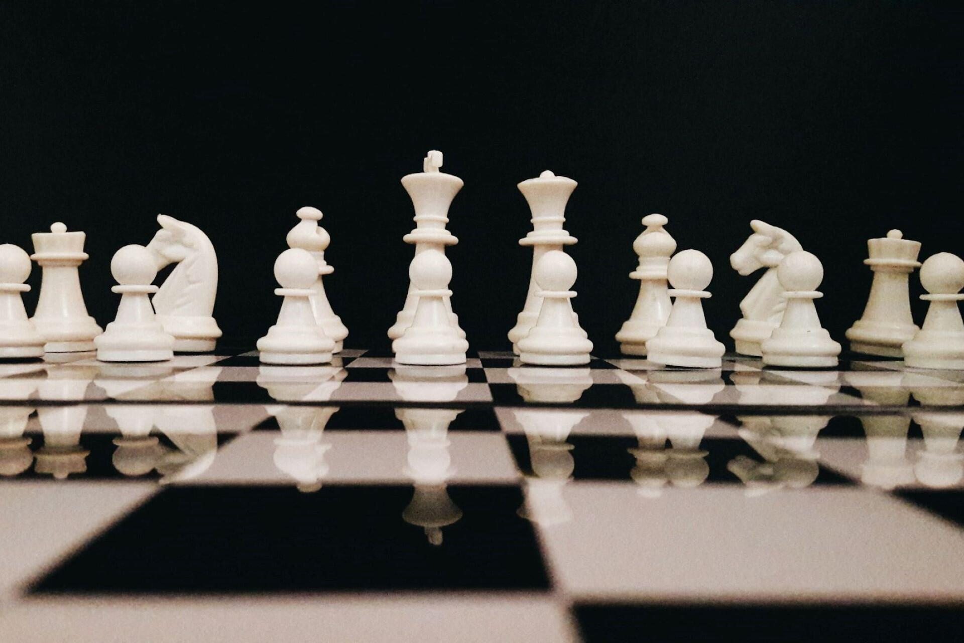 White chess pieces lined up on a chessboard at the start of a game with king, queen, knights, and pawns visible.
