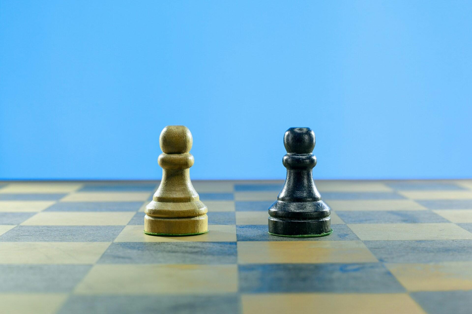 White and black pawn pieces facing each other on a chessboard against a blue background